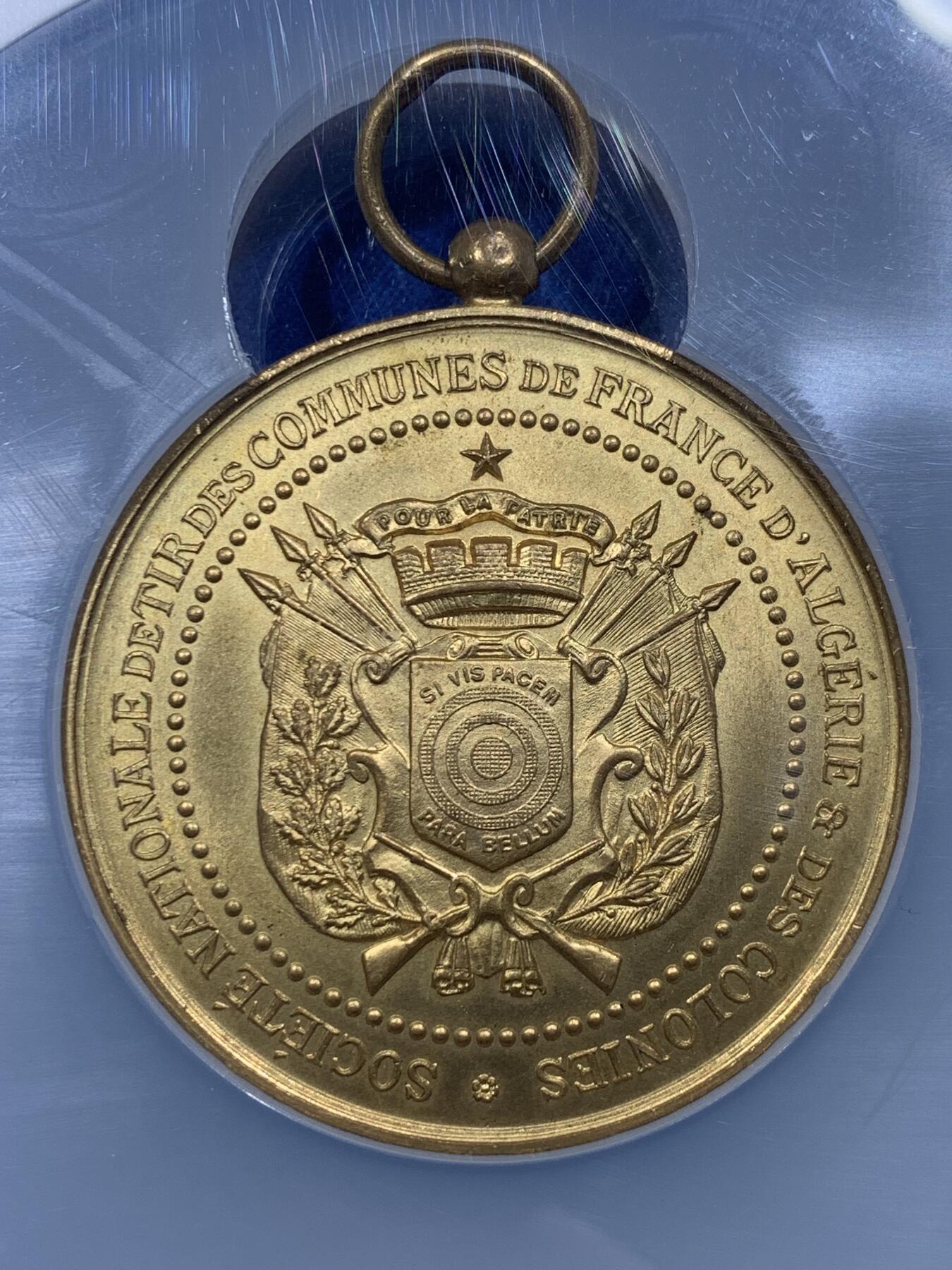 《竞宝斋》第444场 周日，周一，2场连拍 （全场包邮） NGC MS64 约1890年代 法属阿尔及利亚殖民地 射击节镀金大铜章，欧洲射击节常见，殖民地射击节非常稀少。经典的玛丽安娜女神+女性天使，华丽优雅。金水很足，镀层极好。加大加厚盒装，收藏级品质