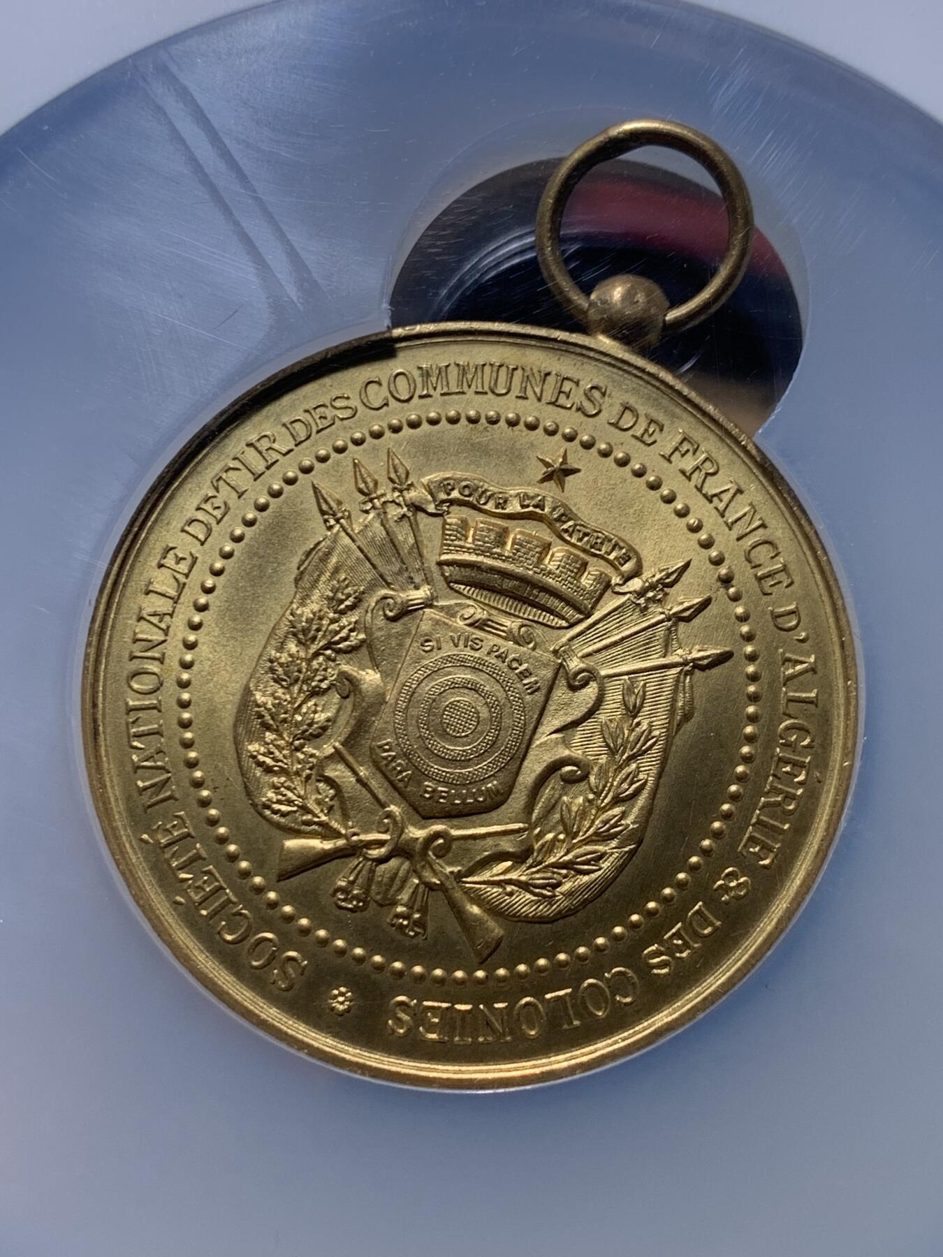 《竞宝斋》第444场 周日，周一，2场连拍 （全场包邮） NGC MS64 约1890年代 法属阿尔及利亚殖民地 射击节镀金大铜章，欧洲射击节常见，殖民地射击节非常稀少。经典的玛丽安娜女神+女性天使，华丽优雅。金水很足，镀层极好。加大加厚盒装，收藏级品质