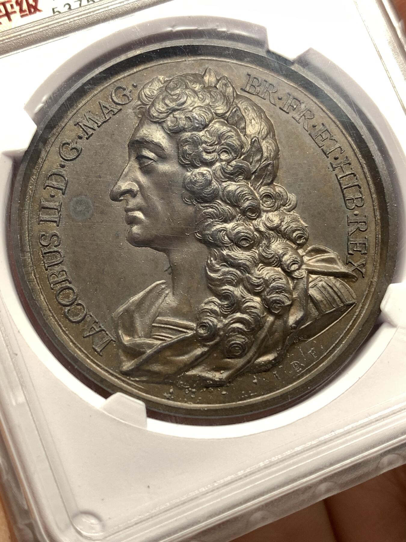 《竞宝斋》第446场 周日，周一，2场连拍 （全场包邮） 华夏 MS62 英王詹姆斯二世纪念铜章，英国历代君主纪念铜章系列之斯图亚特王朝末代国王詹姆斯二世，目录编号：Eimer 384。著名雕模大师瑞士人Dassier的作品，此版属于在整个英王系列里很受欢迎的热门国王品种。开放式盒评级，高浮雕艺术性很强，全面氧化形成“巧克力”色包浆，底板细腻光洁，呈现类精制工艺状态！