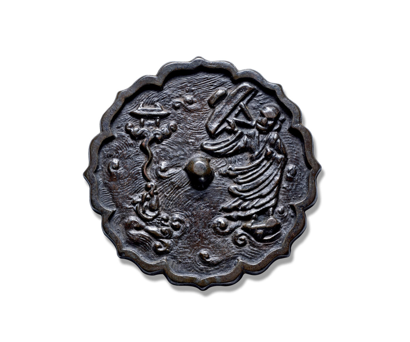 上海匡时2025年秋季拍卖会 中国历代钱币 铜镜专场 达摩渡海镜 八出菱花形，圆钮。此镜整体以水波纹为地纹，水纹以曲线造型，波纹旋转，表现出风急浪大的情景。镜钮右侧一僧人身披袈裟浮于水面，双目凝视远方，左手弯曲，右手持斗笠斜举，脚踏法器御风前行，袍袖随风飘动。镜钮左侧水中浮起一鳌鱼喷吐的水花中升腾起一座小庙，纹饰构图具有丰富的想象力。镜背纹饰描绘了佛教达摩祖师跨海东渡的情景。达摩祖师是天竺香至王子，婆罗门种姓的第二十八代佛徒，南朝梁武帝大通元