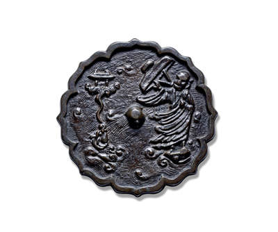 上海匡时2025年秋季拍卖会 中国历代钱币 铜镜专场 - 达摩渡海镜 八出菱花形，圆钮。此镜整体以水波纹为地纹，水纹以曲线造型，波纹旋转，表现出风急浪大的情景。镜钮右侧一僧人身披袈裟浮于水面，双目凝视远方，左手弯曲，右手持斗笠斜举，脚踏法器御风前行，袍袖随风飘动。镜钮左侧水中浮起一鳌鱼喷吐的水花中升腾起一座小庙，纹饰构图具有丰富的想象力。<br>镜背纹饰描绘了佛教达摩祖师跨海东渡的情景。达摩祖师是天竺香至王子，婆罗门种姓的第二十八代佛徒，南朝梁武帝大通元