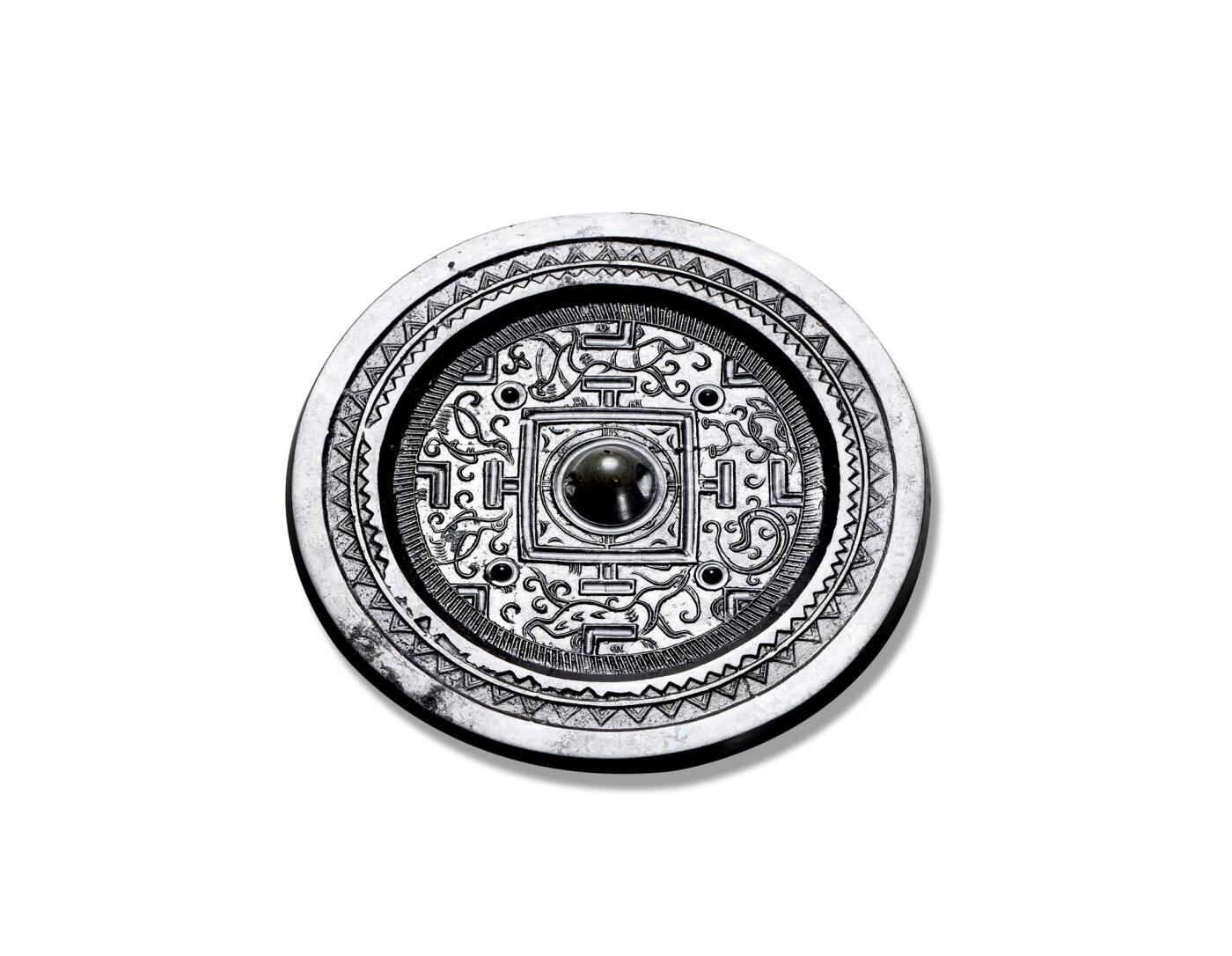 上海匡时2025年秋季拍卖会 中国历代钱币 铜镜专场 神兽规矩镜 圆形，圆钮。双线凹面界格和规矩纹将镜背分成四方。内饰有瑞兽，且有四枚圆座乳丁配饰。瑞默纹精密细腻，造型生动。宽镜缘，饰以锯齿纹与双线齿纹各一圈。镜体黑亮，版模光气上佳，纹饰线条流畅，刻画尤为生动。