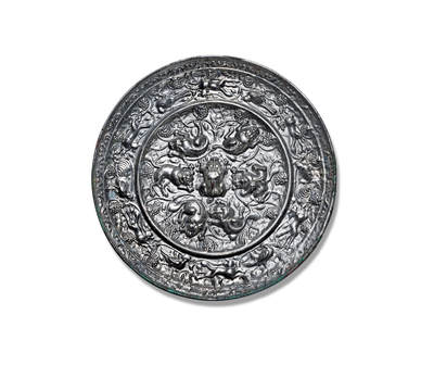 上海匡时2025年秋季拍卖会 中国历代钱币 铜镜专场 - 海兽葡萄镜 圆形，伏兽钮。伏兽形体丰腴，造型精巧，神态刻画清晰，风格富丽华美。镜背以凸棱划分为内外两区：内区环饰六只姿态各异的瑞兽，浮雕立体感强，构图富于变化，情态生动，将具有情节性的画面巧妙融入装饰意趣之中，艺术表现力突出。瑞兽周围葡萄叶蔓缠绕，共同营造出一幅悠然恬静、生机盎然的自然景致。外区饰以跑兽与瑞鸟，掩映于繁密的葡萄枝蔓与果实之间。瑞兽体态丰盈灵动，禽鸟翎羽飘逸，姿态优雅挺拔。果实累累，