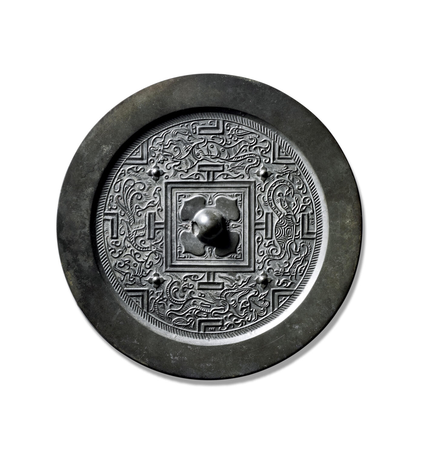 上海匡时2025年秋季拍卖会 中国历代钱币 铜镜专场 四神规矩镜 圆形，圆钮，柿蒂纹钮座，叶尖各饰一卷叶纹。双线凹面方格四角外饰四枚四叶纹座乳钉与博局纹将主纹饰分为四方八区，内饰四组禽兽，隔T形符号相背。青龙区域，羽人持灵芝、仙龟衔仙草；白虎区域，狗熊戏白虎；朱雀区域，羽人献花草；玄武区域，仙鹿衔仙草；朱雀区域，羽人献花草。主纹间填以雀鸟纹与云气纹，主纹外饰一周栉齿纹。素宽缘，黑漆古，品相佳。