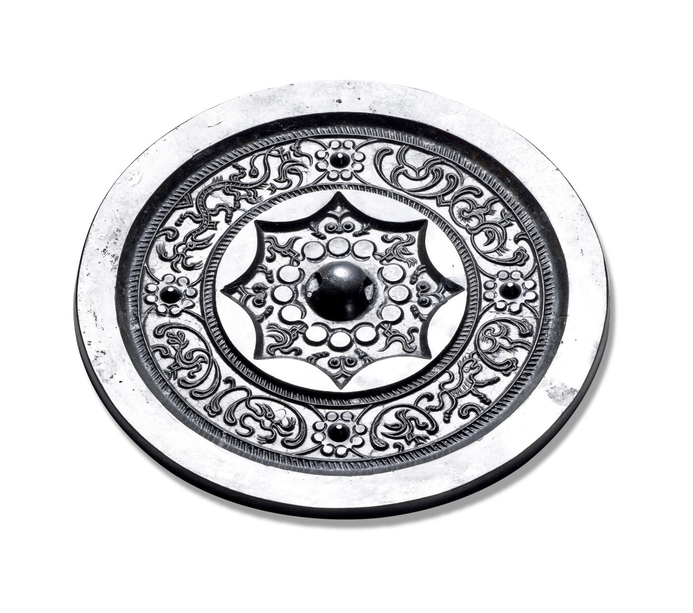 上海匡时2025年秋季拍卖会 中国历代钱币 铜镜专场 四乳变形凤纹镜 圆形，圆钮。十二连珠纹底座钮座外饰四凤鸟纹及乳钉草叶纹，钮座外有一周栉齿纹与一周内向八连孤，主纹饰为八连珠纹底座四乳钉间饰八组用弧线勾勒的抽象鸟纹图形，周边一周栉齿纹，素面宽缘。此镜图形怪异夸张，镖修条婉转繁缛，通体黑漆古，亮可鉴人。