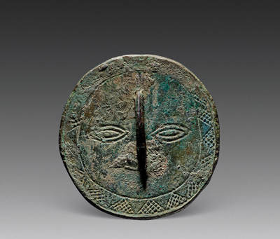 上海匡时2025年秋季拍卖会 中国历代钱币 铜镜专场 - 太阳神纹镜 不规则圆形，鼻形钮。主纹饰为造型古朴的一张人面纹，圆脸凤眼，双目炯炯有神，桥钮为鼻，钮下纹饰为嘴，外围两周圈带中间饰锯齿纹，形成太阳光芒纹，其外填满鱼子点纹。若作太阳崇拜理解时，人脸即是太阳神，锯齿应系太阳光芒，鱼子点似为「满天星星」。整个人脸呆萌天真，造型抽象又形象，具有鲜明的地域与时代特征，品种极为少见，此枚纹饰仅见，包浆熟润，保存完整。<br>来源：台北“一雅堂”旧藏。<br>参