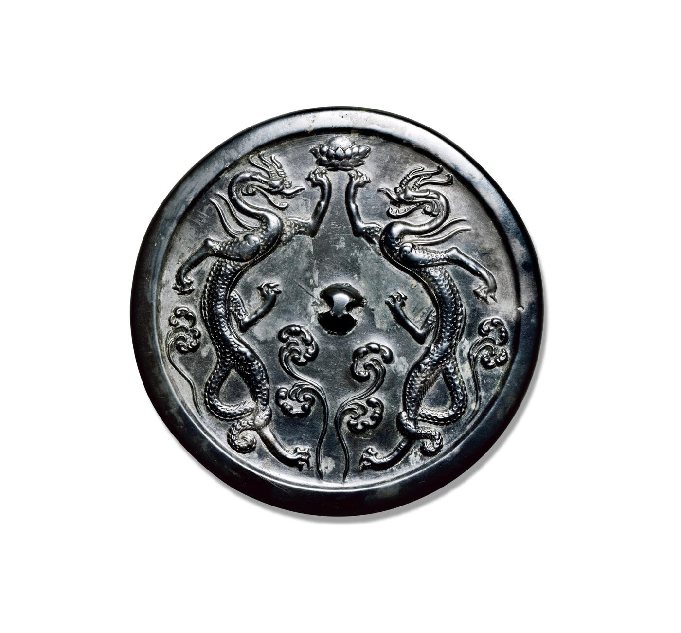 上海匡时2025年秋季拍卖会 中国历代钱币 铜镜专场 双龙镜 圆形，圆钮。镜背主题纹饰为双龙隔钮相对，身修长，四肢伸张，呈跃欲动飞跃之势。龙首上方，各举前肢，共托宝莲。龙纹整体造型巧妙，布局饱满。纹饰刻画细腻入微，龙首犄角分明，五官清晰可见，神态鲜活，张口吐舌，双目直视，鳞甲清晰，背鳍、腹甲、鳞片、龙尾均刻画细密，龙爪劲健，伸向四方。强健的龙体和修长的四肢具有独特卓异的动律美、节奏美和力度美。背铸龙纹若凌空腾起，犹似白居易「背有九五飞天龙，人