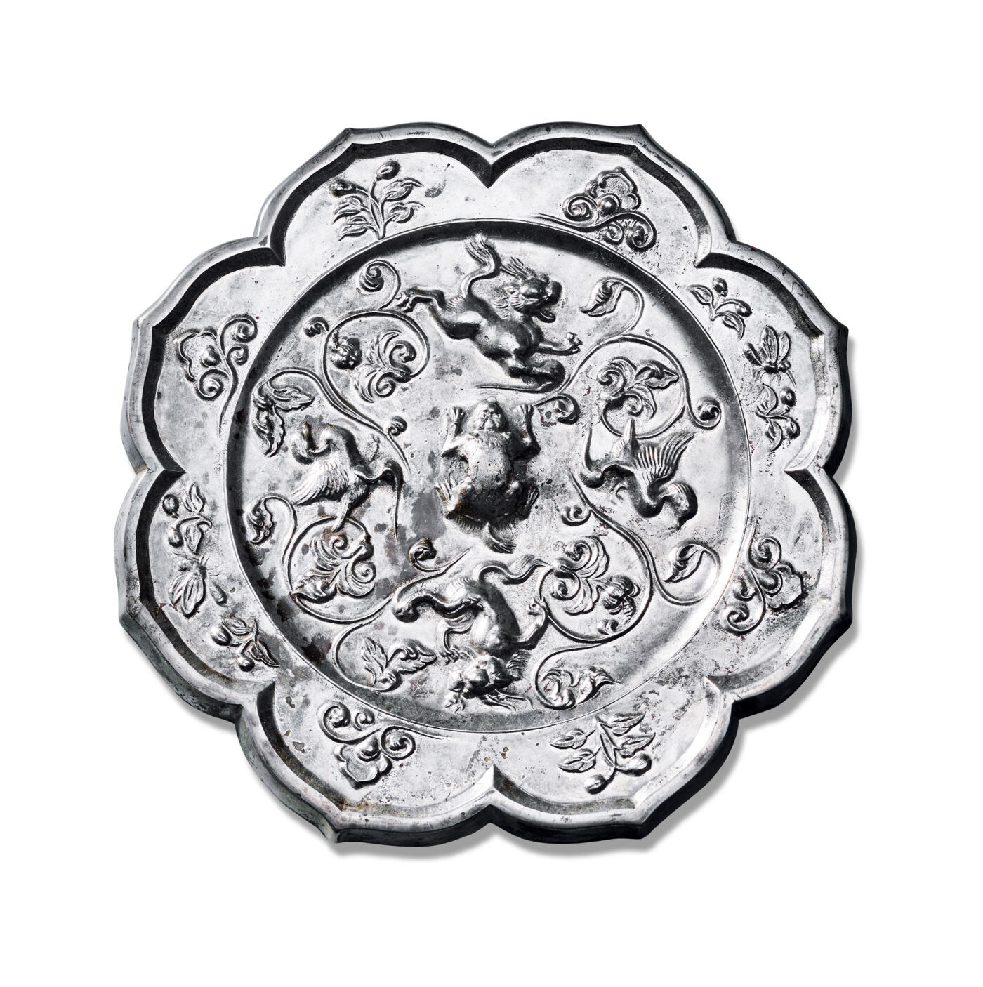 上海匡时2025年秋季拍卖会 中国历代钱币 铜镜专场 镂空腿双鸳鸯双狮镜 八出菱花形，伏兽钮。主题纹饰分为四区，两对展翅鸳鸯与两头咆哮跳跃的狮子相间排列，其间饰以四组缠枝花卉。鸳鸯羽翼舒展，姿态飘逸；瑞兽形体丰硕，动作夸张，张口怒吼，神态生动。缠枝花卉婉转流畅，衬托出富丽华贵之气。镜缘饰以祥云与花枝纹，清新婉约，自然优美。此镜铸造工艺精湛，风格富丽华美。镜体泛银白光，熠熠生辉，整体画面生机盎然，自由活泼中见矫健挺拔之美，彰显出盛世时期丰腴华丽的审美趣