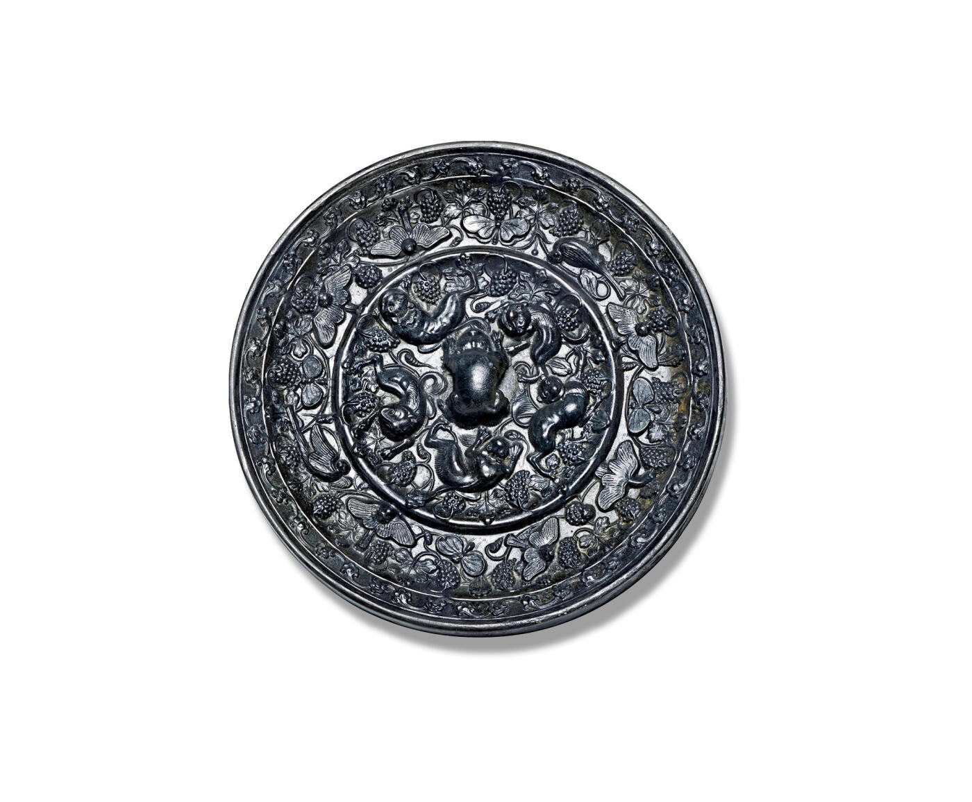 上海匡时2025年秋季拍卖会 中国历代钱币 铜镜专场 海兽葡萄镜 圆形，伏兽钮。弦纹高圈将镜背分为内外两区：内区五只瑞兽环绕镜钮攀援嬉戏，多作匍匐姿态，其间点缀葡萄叶蔓与果实；外区饰有一周造型各异的禽鸟与蝴蝶，或飞翔或栖息于葡萄藤蔓之间，果实累累，更添生机。镜缘饰以花卉纹。此镜版工极为精细，属头版头模，铜质精良，黑漆古皮壳，保存完整，体积虽小却属精品，极具收藏价值，惜裂修。