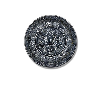 上海匡时2025年秋季拍卖会 中国历代钱币 铜镜专场 - 海兽葡萄镜 圆形，伏兽钮。弦纹高圈将镜背分为内外两区：内区五只瑞兽环绕镜钮攀援嬉戏，多作匍匐姿态，其间点缀葡萄叶蔓与果实；外区饰有一周造型各异的禽鸟与蝴蝶，或飞翔或栖息于葡萄藤蔓之间，果实累累，更添生机。镜缘饰以花卉纹。此镜版工极为精细，属头版头模，铜质精良，黑漆古皮壳，保存完整，体积虽小却属精品，极具收藏价值，惜裂修。