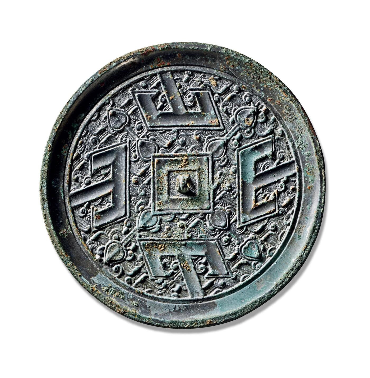 上海匡时2025年秋季拍卖会 中国历代钱币 铜镜专场 四山镜 圆形，三弦钮，方钮座。外围饰方形凹面环带以象征大地，与象征苍天的圆形镜体相呼应，体现了古人“天圆地方”的宇宙观念。方框四角各伸出一组花叶纹。主题纹饰为四组“山”字纹与羽状地纹相结合的复合纹样，主纹方正庄重，地纹细密秀丽，两者层次分明，布局严谨。四组“山”字纹呈左旋排列，其中间竖笔顶端抵于镜缘。此镜保存完好，状态极佳。