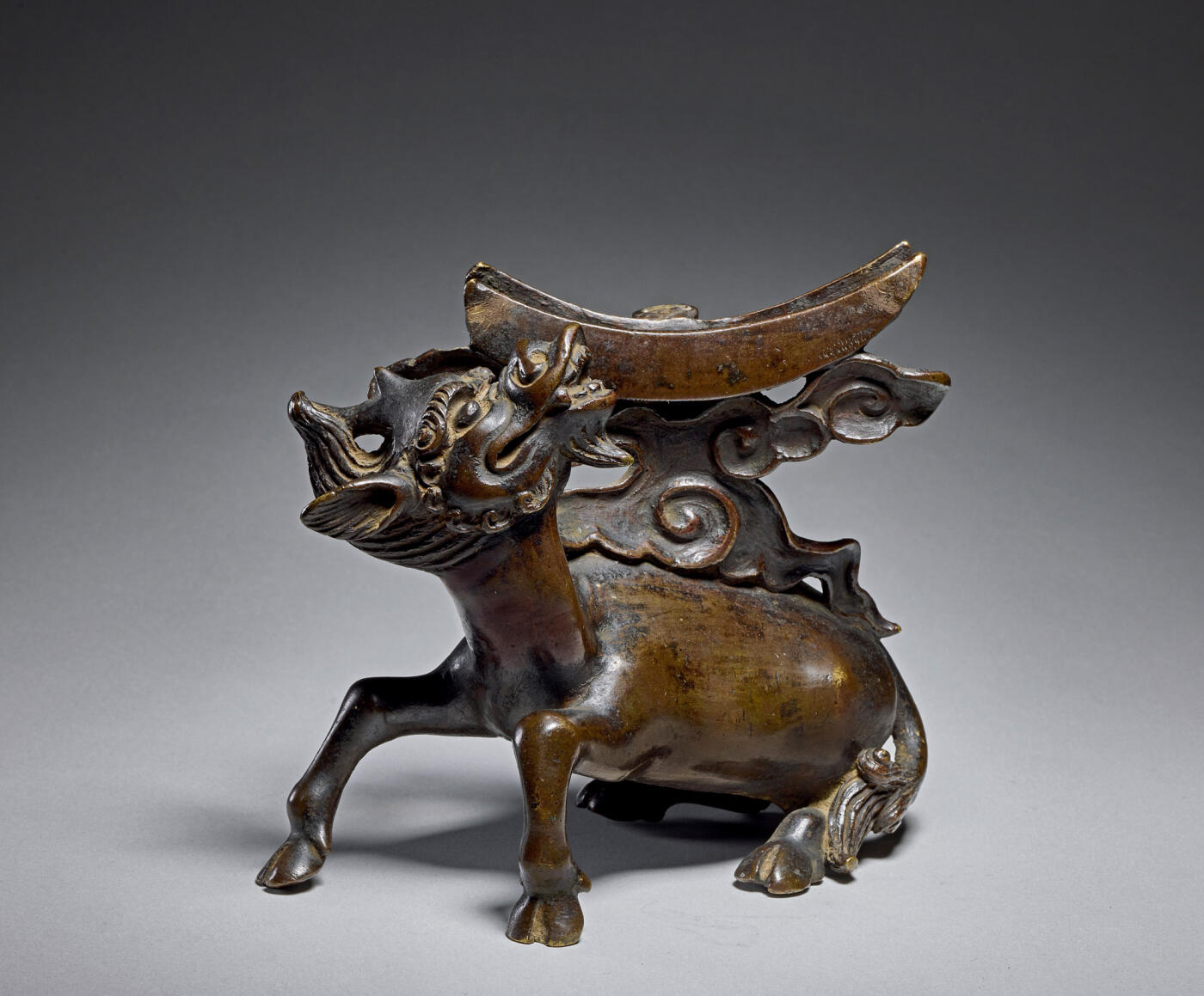 上海匡时2025年秋季拍卖会 中国历代钱币 铜镜专场 犀牛望月镜架 铜制镜架，整体呈犀牛望月状，犀牛作自然回首跪卧状，犀牛背上祥云凸起，托起一个弯月形的用来搁靠铜镜的部件，祥云和弯月之间有空槽，摆放铜镜时，只要将铜镜插入空槽之中，铜镜便稳稳地靠在弯月形的部件上。此镜架铸造精良，造型生动可爱，保存状态完好。