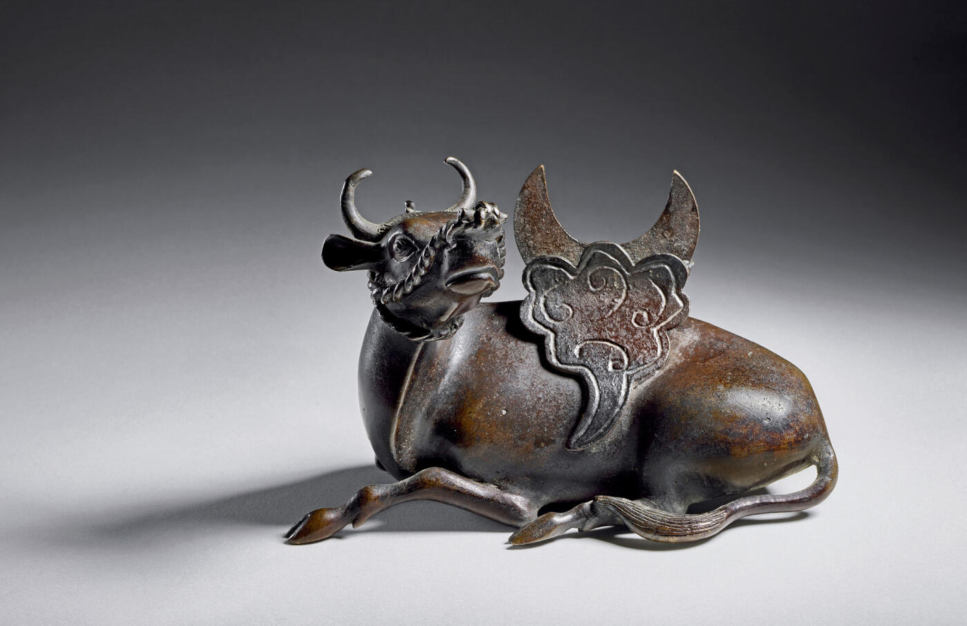 上海匡时2025年秋季拍卖会 中国历代钱币 铜镜专场 犀牛望月镜架 铜质，镜架整体呈犀牛望月状，鎏金犀牛作自然回首跪卧状，犀牛背上祥云凸起，托起一个弯月形的用来搁靠铜镜的部件，祥云和弯月之间有空槽，摆放铜镜时，只要将铜镜插入空槽之中，铜镜便稳稳地靠在弯月形的部件上。此镜架铸造精良，造型生动可爱，保存状态完好。