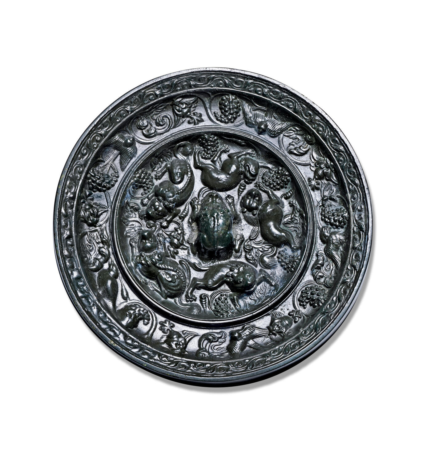 上海匡时2025年秋季拍卖会 中国历代钱币 铜镜专场 海兽葡萄镜 圆形，伏兽钮。瑞兽脊梁凸起，毛发刻画极为精细。一周凸起的高圈将镜背分为内外两区：内区五只瑞兽环绕镜钮，其造型如狐似狼，或回首顾盼，或昂首阔步，形态各异，浑厚生动，意趣盎然。瑞兽间饰以葡萄果实及缠绕穿插的枝叶纹饰，线条优美，布局灵动。外区葡萄藤蔓与禽鸟相间分布，禽鸟或展翅飞舞，或驻足栖息，构图精巧细密。此镜版模清晰，品相上佳。