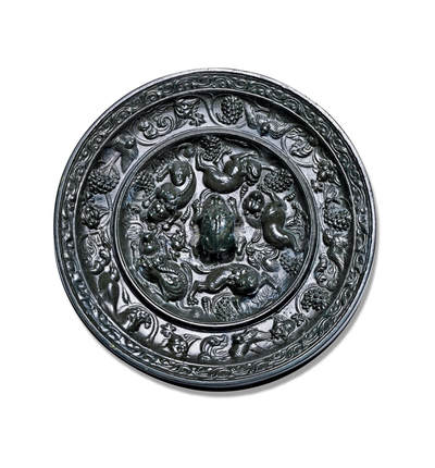 上海匡时2025年秋季拍卖会 中国历代钱币 铜镜专场 - 海兽葡萄镜 圆形，伏兽钮。瑞兽脊梁凸起，毛发刻画极为精细。一周凸起的高圈将镜背分为内外两区：内区五只瑞兽环绕镜钮，其造型如狐似狼，或回首顾盼，或昂首阔步，形态各异，浑厚生动，意趣盎然。瑞兽间饰以葡萄果实及缠绕穿插的枝叶纹饰，线条优美，布局灵动。外区葡萄藤蔓与禽鸟相间分布，禽鸟或展翅飞舞，或驻足栖息，构图精巧细密。此镜版模清晰，品相上佳。