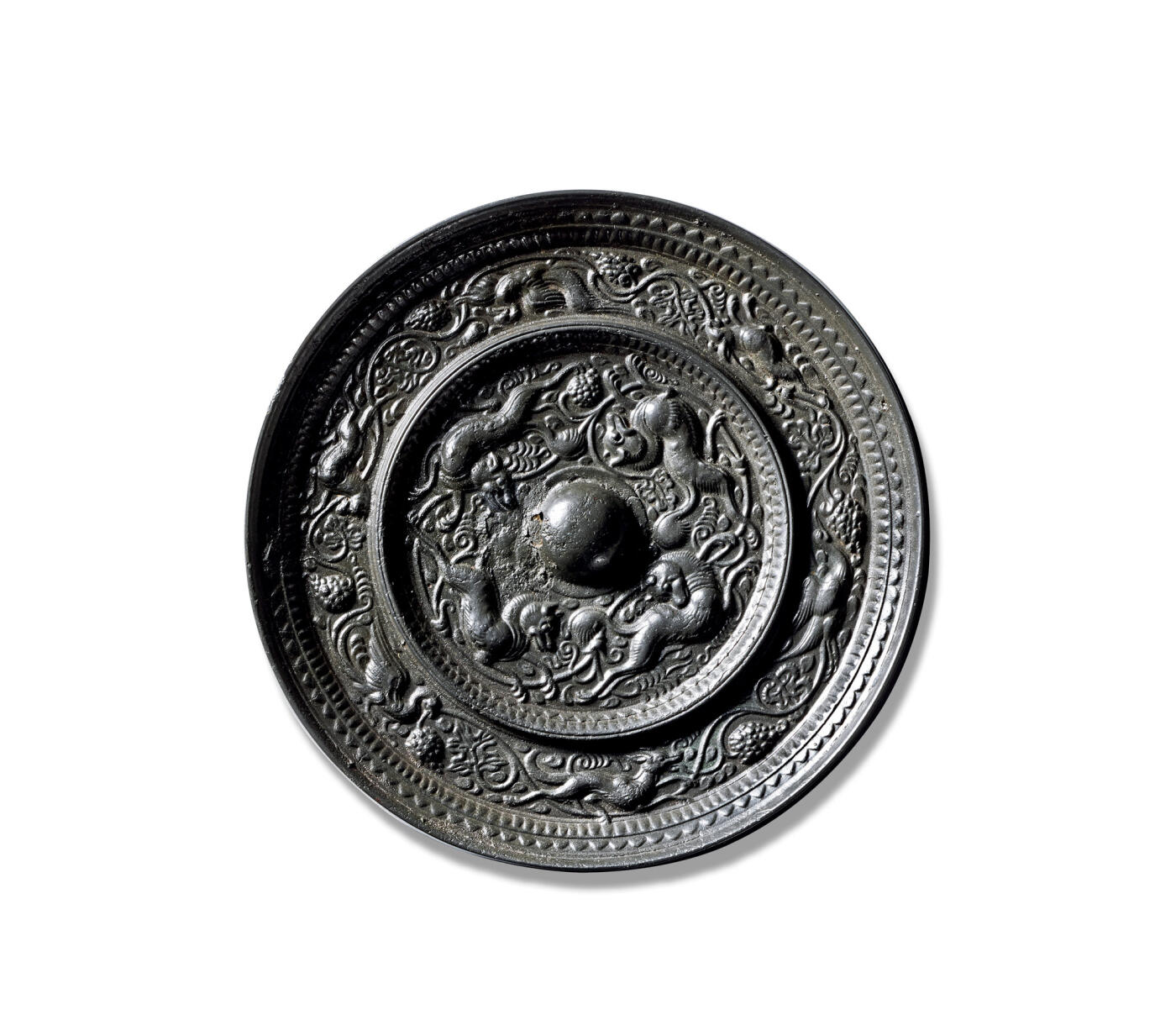 上海匡时2025年秋季拍卖会 中国历代钱币 铜镜专场 瑞兽葡萄纹镜 圆形，圆钮。镜背由一圈高耸的凸棱分隔为内外两区：内区四只瑞兽环钮而踞，身形修长，矫健灵动，或奔或跃，姿态生动；其间葡萄藤蔓蜿蜒盘曲，叶片舒展，果实垂挂，与瑞兽相映成趣。外区则以连绵枝蔓贯穿一周，飞禽、走兽穿梭其间，嬉戏游憩，构成一幅生机盎然的图景。镜缘处饰一周锯齿纹，缘壁窄而高挺。此镜品相上佳，包浆莹润，光泽熠熠。瑞兽飞禽在刻画精妙的葡萄藤蔓间追逐飞舞，画面饱满而富有动感，展现出极高