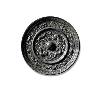 上海匡时2025年秋季拍卖会 中国历代钱币 铜镜专场 - 瑞兽葡萄纹镜 圆形，圆钮。镜背由一圈高耸的凸棱分隔为内外两区：内区四只瑞兽环钮而踞，身形修长，矫健灵动，或奔或跃，姿态生动；其间葡萄藤蔓蜿蜒盘曲，叶片舒展，果实垂挂，与瑞兽相映成趣。外区则以连绵枝蔓贯穿一周，飞禽、走兽穿梭其间，嬉戏游憩，构成一幅生机盎然的图景。镜缘处饰一周锯齿纹，缘壁窄而高挺。此镜品相上佳，包浆莹润，光泽熠熠。瑞兽飞禽在刻画精妙的葡萄藤蔓间追逐飞舞，画面饱满而富有动感，展现出极高