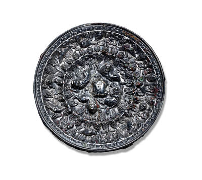 上海匡时2025年秋季拍卖会 中国历代钱币 铜镜专场 - 海兽葡萄镜 圆形，伏兽钮。镜背空间由一周凸棱划分为内外两区。内区环绕镜钮饰有四只昂首趴伏的海兽，形体饱满，刻画精细，姿态憨拙可掬；其间满铺细密交错的葡萄果实与枝蔓，枝蔓延伸跨越凸梁进入外区，形成所谓“过梁葡萄”的独特构图。外区在繁茂的葡萄藤蔓间点缀四只展翅飞翔的禽鸟，动静相宜，生意盎然，俨然一幅充满生趣的乐园图景。镜缘饰有一周卷叶纹。