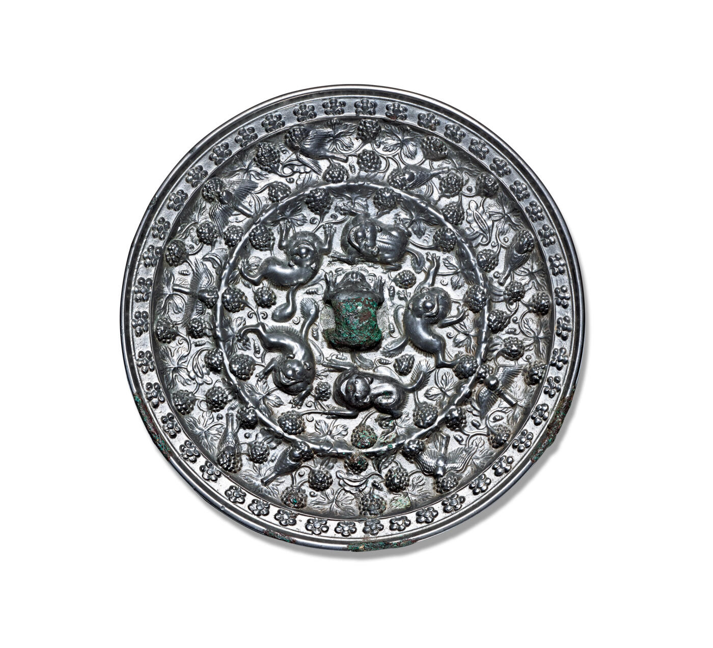 上海匡时2025年秋季拍卖会 中国历代钱币 铜镜专场 海兽葡萄镜 圆形，伏兽钮。镜背由一周轮脊分为内外两区：内区装饰五只浮雕瑞兽，姿态各异，形体矫健，其间以葡萄枝蔓图案为地纹；外区饰有形态各异的鸟雀纹。内区的葡萄藤蔓纹蜿蜒越过轮脊延伸至外区，形成鸟雀穿飞于藤蔓间的生动画面。镜缘高平凸起，饰一周团花图案。此镜通体银光莹润，锈色古朴自然，镜形厚重大气，纹饰繁复错落，极具富丽华美之气象。