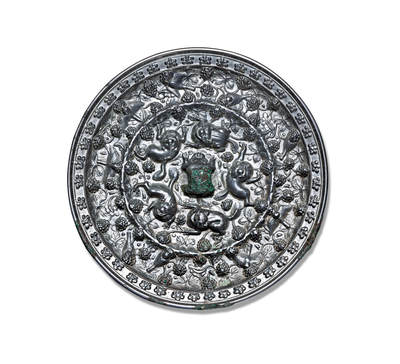 上海匡时2025年秋季拍卖会 中国历代钱币 铜镜专场 - 海兽葡萄镜 圆形，伏兽钮。镜背由一周轮脊分为内外两区：内区装饰五只浮雕瑞兽，姿态各异，形体矫健，其间以葡萄枝蔓图案为地纹；外区饰有形态各异的鸟雀纹。内区的葡萄藤蔓纹蜿蜒越过轮脊延伸至外区，形成鸟雀穿飞于藤蔓间的生动画面。镜缘高平凸起，饰一周团花图案。此镜通体银光莹润，锈色古朴自然，镜形厚重大气，纹饰繁复错落，极具富丽华美之气象。