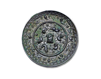 上海匡时2025年秋季拍卖会 中国历代钱币 铜镜专场 - 海兽葡萄镜 圆形，伏兽钮。镜背由一圈凸梁分隔为内外两区。内区饰高浮雕瑞兽六只，环钮而踞，姿态各异：或回首顾盼，或昂首前行，造型顽皮生动，极富自然意趣。内外区均满铺葡萄藤蔓纹饰，果实饱满，枝叶扶疏，藤蔓虬曲蜿蜒，布局繁密而不失灵动，细腻中见生机。镜缘高耸，缘面缓倾，上饰连续排列的卷云，为整体增添庄重与韵律之美。