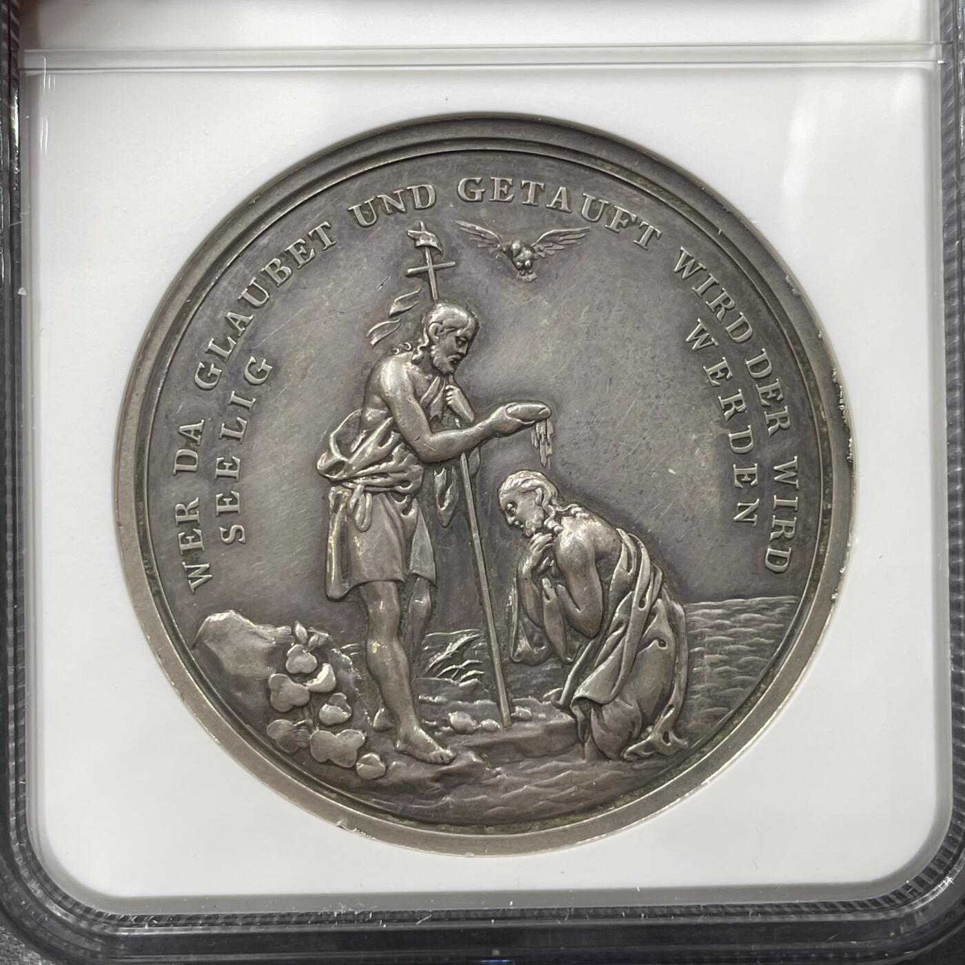 「木头集藏」“冬至雅藏”——章牌精品专场！ 德国耶稣受洗银章，MS 61,直径：42mm，34.6g，少见银章！正面刻画耶稣受洗场景：施洗约翰为耶稣施洗，上方有象征圣灵的白鸽，这是基督教经典的宗教题材，还原了《圣经》中耶稣在约旦河受洗的情节。背面德语铭文SEELIG WER DA GLAUBET UND GETAUFT WIRD，直译是“信而受洗的人，必然得救”，这句话出自《马可福音》，是基督教关于洗礼与救赎的核心教义之一。