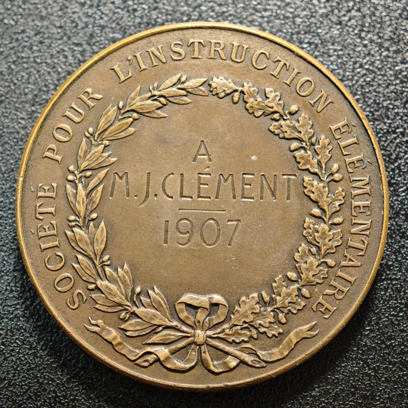 【德藏】世界币章拍卖第158期（拍品征集中~欢迎藏友联系） 1907年 法国初级教育协会纪念铜章，1815年版本，正面是三个坐着的小孩子正在书写板上做记录，站着天使指着墙上挂着的三块中间的牌子正在教导他们；背面是月桂和橡木枝组成的花环和铭文 直径约：41.2mm；重约：37.6g