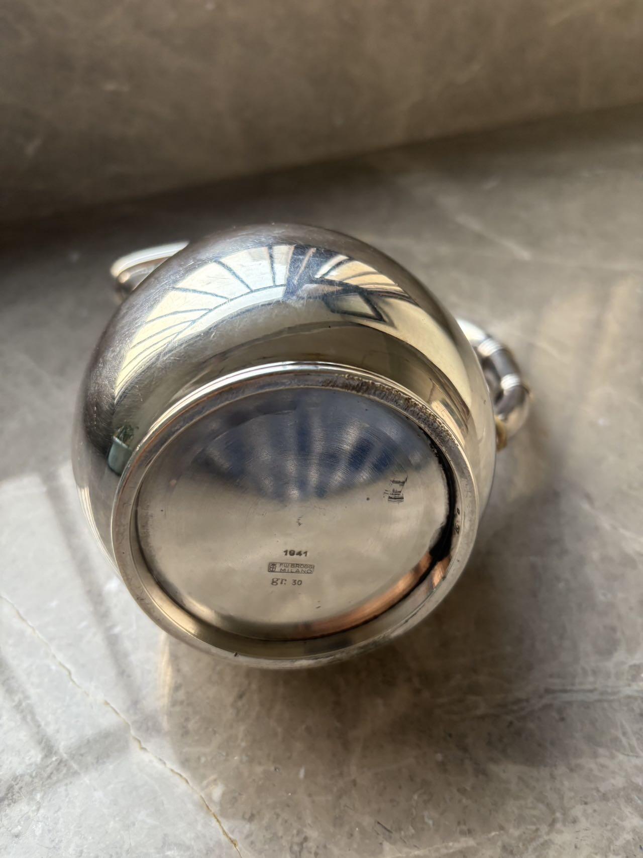 盛世勋华——号角文化勋章邮票专场拍卖第294期 意大利王国皇家海军1941年军官定制银壶，重989克，由米兰知名工坊Broggi打造，执壶通高220毫米（含把手），采用银制工艺打造（部分镀银），器身经精细錾刻与抛光处理，线条流畅饱满，呈现出优雅的梨形轮廓。壶身饰有意大利皇家海军专属纹章与航海主题装饰纹样，底座有银标和厂标