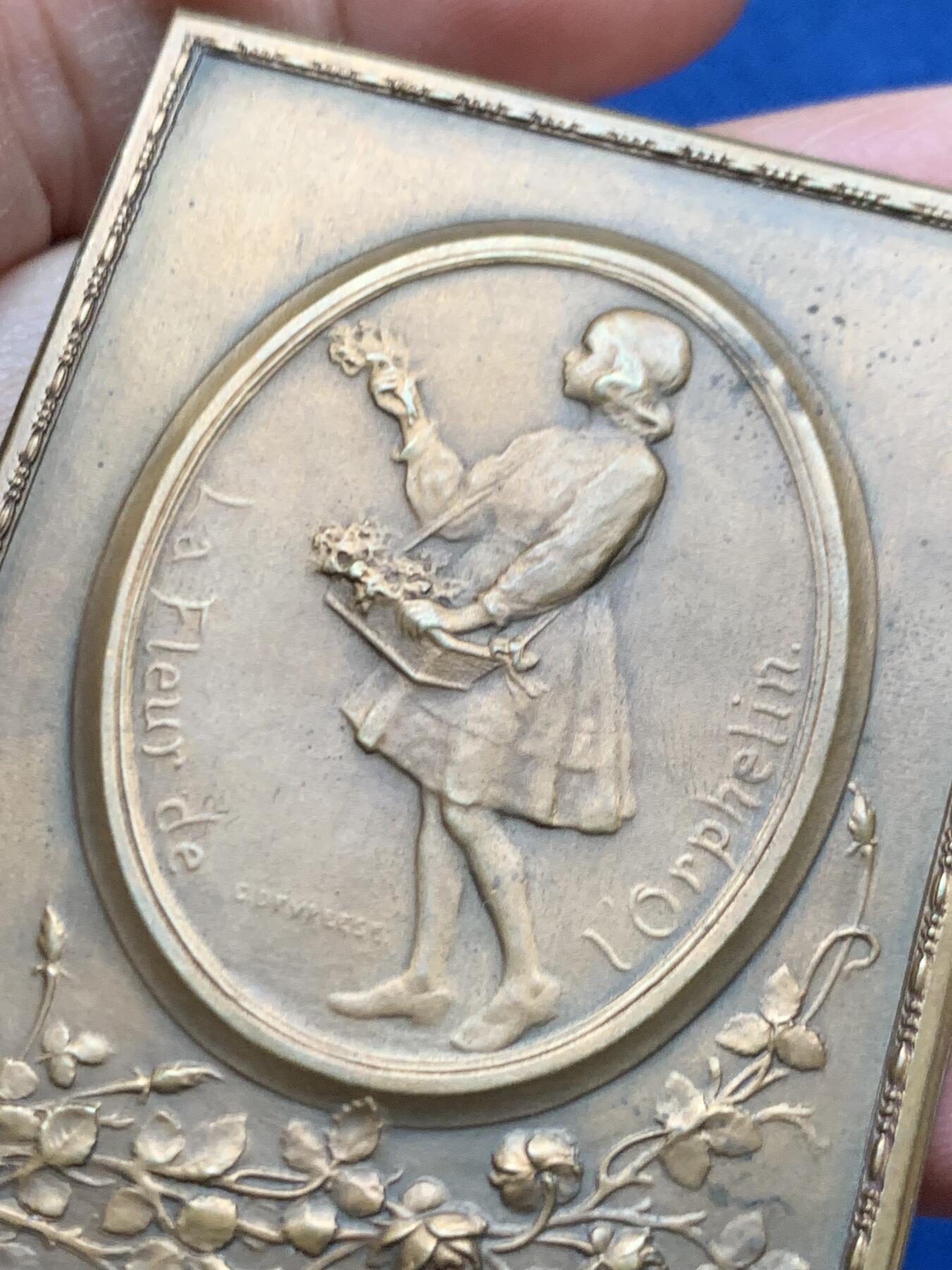 《竞宝斋》第451场 周日，周一，周二  3场连拍 （全场包邮，欢迎送拍） 比利时著名雕刻家：Godefroid Devreese作品-《孤儿之花》艺术奖章，非常漂亮，双面人物雕刻，整体奖章以画框形式展现，极为少见，正面女神展开双臂将儿童拥入怀中，十分暖意。背面一名手提花篮的穿连体短裙的小女儿，手拿花束十分优雅。不可错过。规格：62*46.6mm，重：90.4g