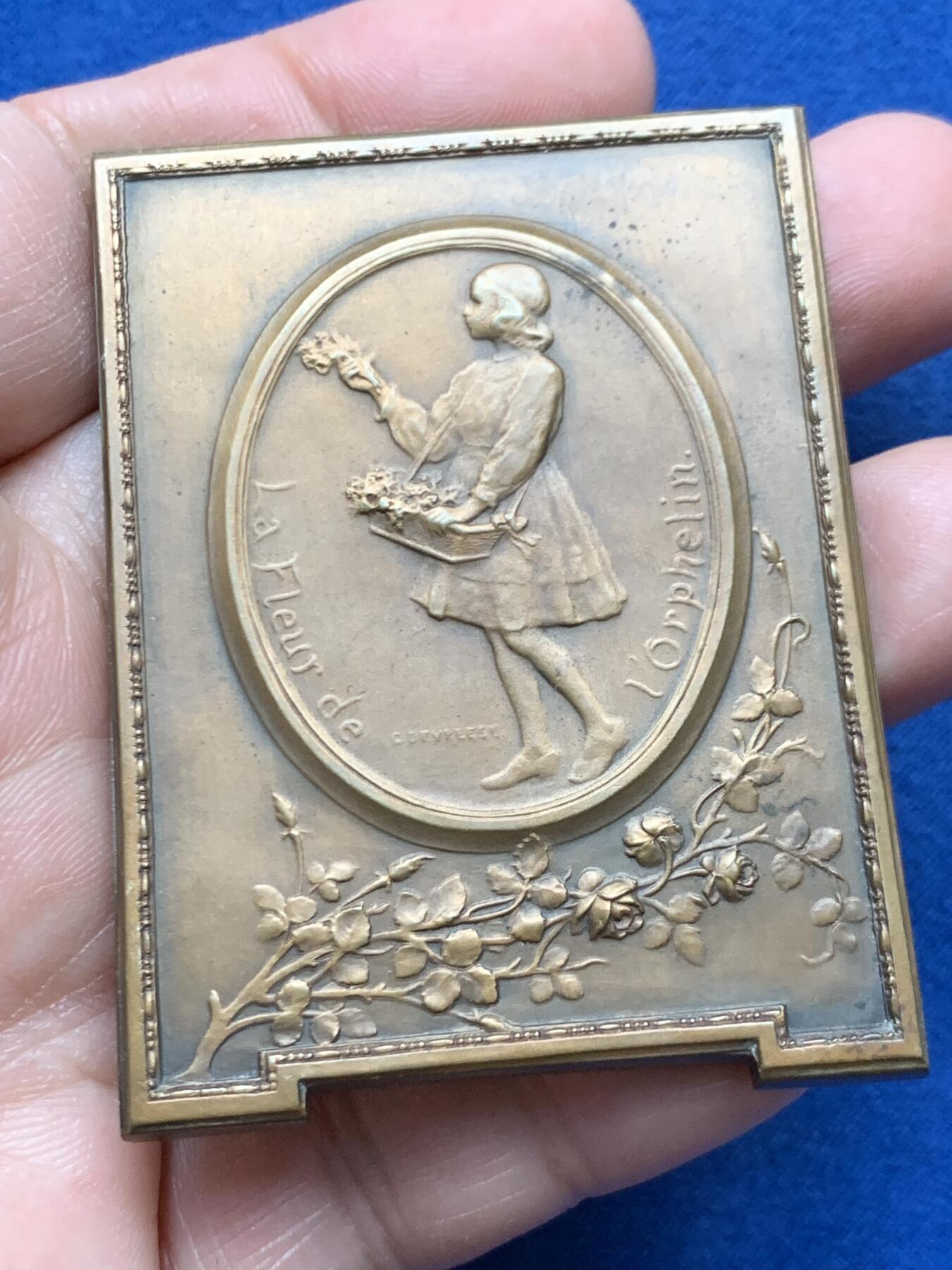 《竞宝斋》第451场 周日，周一，周二  3场连拍 （全场包邮，欢迎送拍） 比利时著名雕刻家：Godefroid Devreese作品-《孤儿之花》艺术奖章，非常漂亮，双面人物雕刻，整体奖章以画框形式展现，极为少见，正面女神展开双臂将儿童拥入怀中，十分暖意。背面一名手提花篮的穿连体短裙的小女儿，手拿花束十分优雅。不可错过。规格：62*46.6mm，重：90.4g