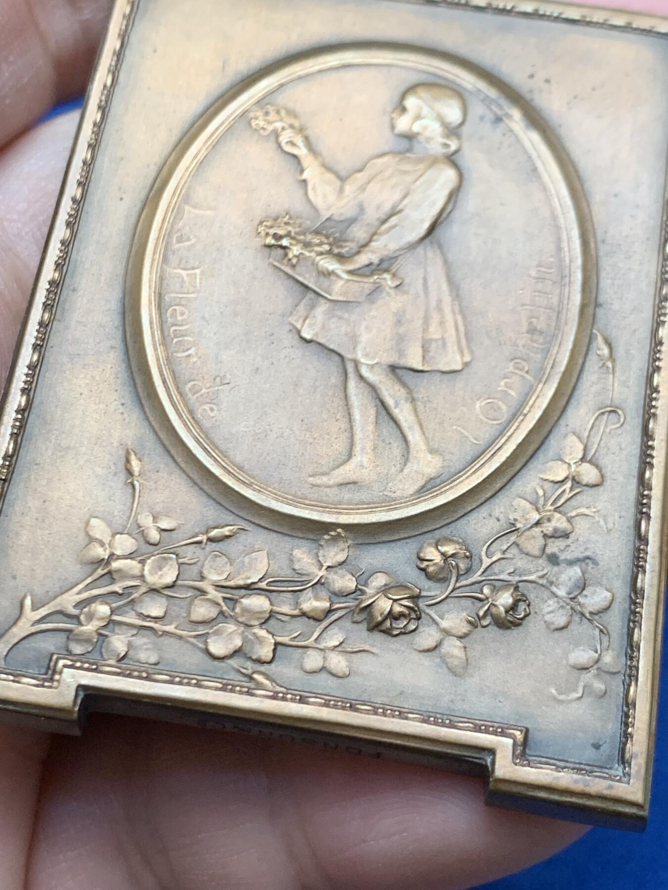 《竞宝斋》第451场 周日，周一，周二  3场连拍 （全场包邮，欢迎送拍） 比利时著名雕刻家：Godefroid Devreese作品-《孤儿之花》艺术奖章，非常漂亮，双面人物雕刻，整体奖章以画框形式展现，极为少见，正面女神展开双臂将儿童拥入怀中，十分暖意。背面一名手提花篮的穿连体短裙的小女儿，手拿花束十分优雅。不可错过。规格：62*46.6mm，重：90.4g