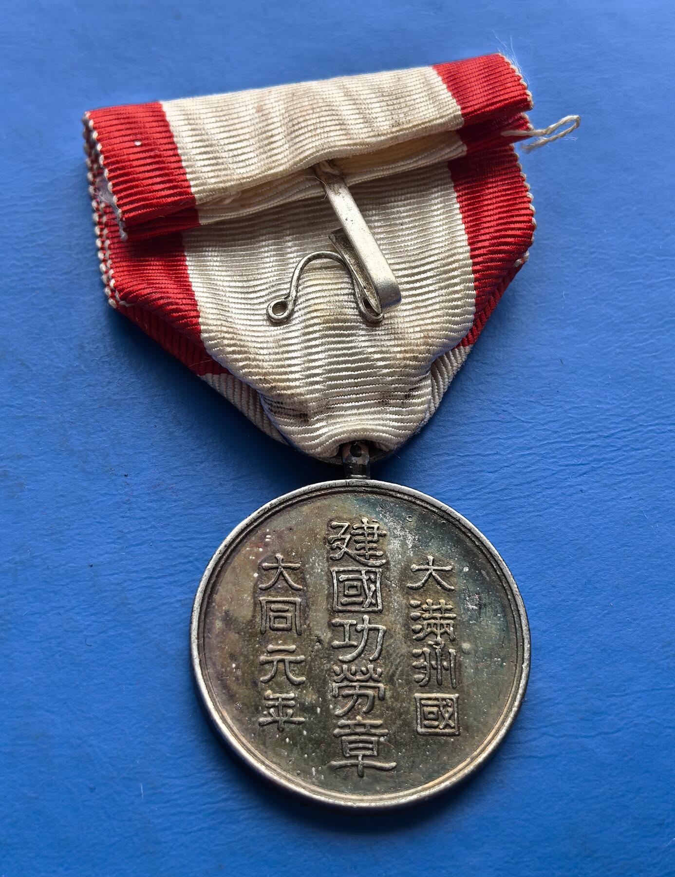 外国优质老铜币高银银币，周六九点倒数截拍，满百包邮，持续收拍 伪满洲国大同元年 “建国功劳章”，刻 “建國” 等字，系殖民罪证，包浆凝史，历史研究与警示的珍稀实物 。长66mm含绶带，宽28.5mm，重13克，材质不明，是否原铸自己辨别，售出不退