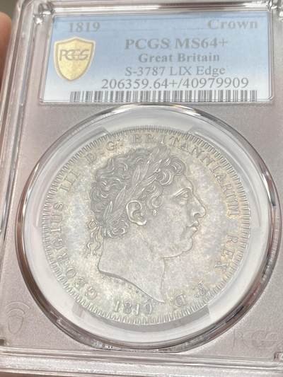 万国钱币拍卖第058期（万国新年大拍） PCGS MS64+ 1819年LIX英国乔治三世马剑克朗大银 英国马剑系列的开山之作 马剑图案由著名的意大利雕刻家Pistrucci设计 在钱币两面皆留下签名 这在当时是难以被接受的（通常只留首字母缩写） 此举也为后来首席雕刻师W.Wyon上位埋下伏笔 此枚无论底板，包浆，还是高点都堪称无可挑剔  一枚乔三马剑的标准器  高分价格越来越看不懂的存在 此次贴脸入手机会切勿错过