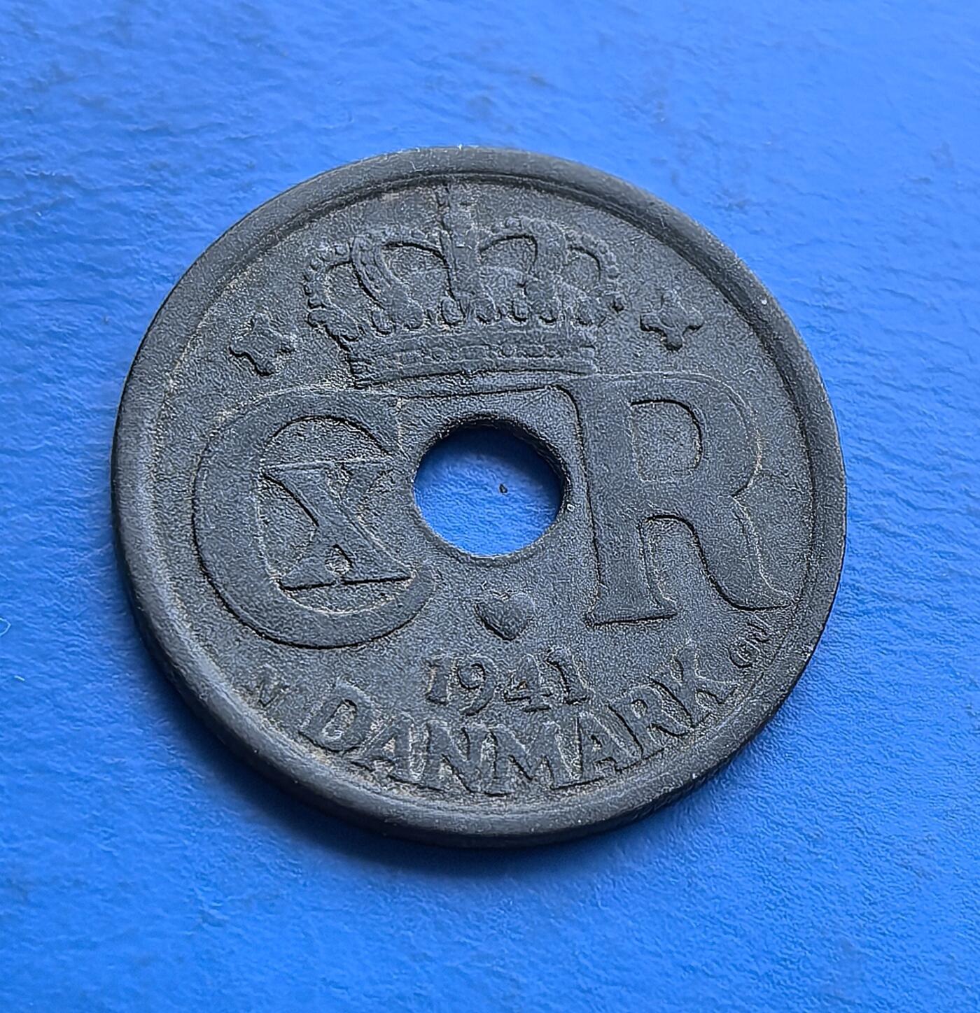 外国优质老铜币高银银币，周六九点倒数截拍，满百包邮，持续收拍 丹麦 1941 年25 欧尔圆孔锌币，铸于二战被占期。正面君主花押（CXR）配皇冠，背面面额嵌螺旋纹，圆孔因资源匮乏而生。锌质包浆凝战时沧桑，见证北欧中立国沦陷下的货币应急。作为二战丹麦币标本，亲民可藏，解码被占期资源困局与王室符号存续 。