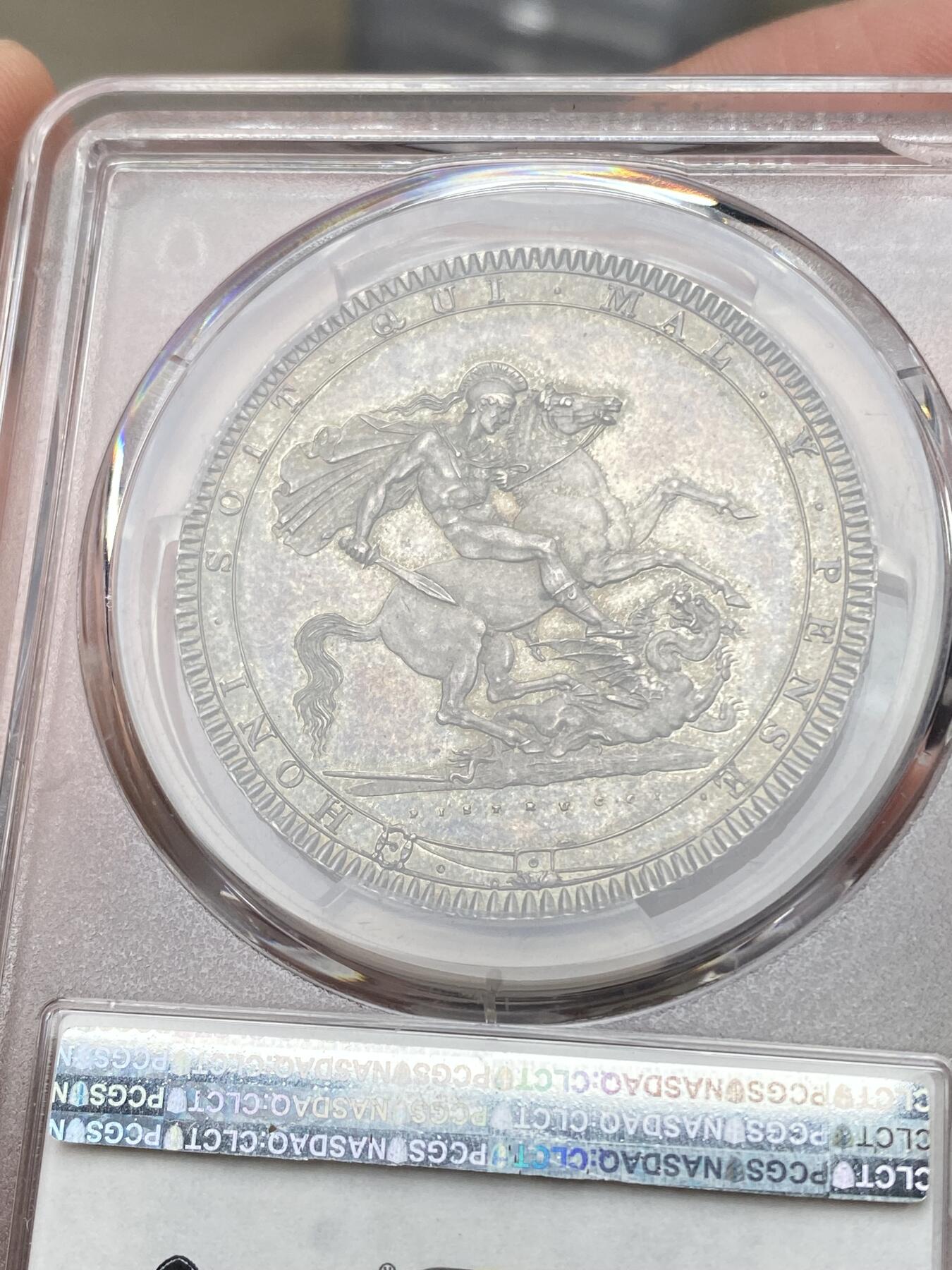 万国钱币拍卖第058期（万国新年大拍） PCGS MS64+ 1819年LIX英国乔治三世马剑克朗大银 英国马剑系列的开山之作 马剑图案由著名的意大利雕刻家Pistrucci设计 在钱币两面皆留下签名 这在当时是难以被接受的（通常只留首字母缩写） 此举也为后来首席雕刻师W.Wyon上位埋下伏笔 此枚无论底板，包浆，还是高点都堪称无可挑剔  一枚乔三马剑的标准器  高分价格越来越看不懂的存在 此次贴脸入手机会切勿错过