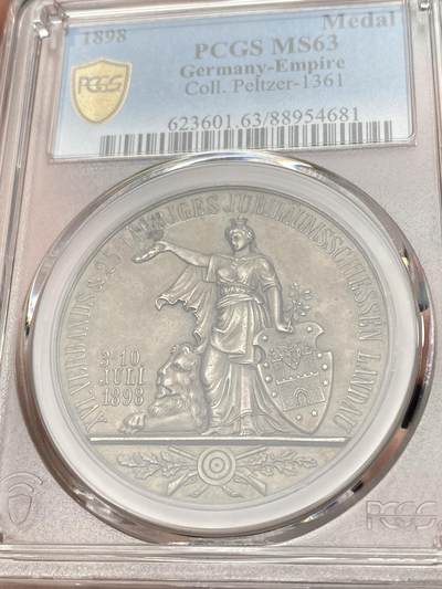 万国钱币拍卖第058期（万国新年大拍） PCGS MS63 1898年德国巴伐利亚兰道-普法尔茨第十六届射击节暨25周年纪念银章 冠军分罕见小邦射击节 正面:日耳曼妮娅女神右手举着胜利桂冠，左手持橡树枝，靠在兰道城市纹章盾徽上，巴伐利亚雄狮趴在她的脚边，底部是射击节标志。背面:王冠，巴伐利亚-兰道-普法尔茨的盾徽，底部是群山中的城市景观，朝阳升起。鸟瞰视角，广阔天地跃然章上。微缩雕刻，极其精细。高浮雕磨砂工艺，热门女神德射，自藏佳品。