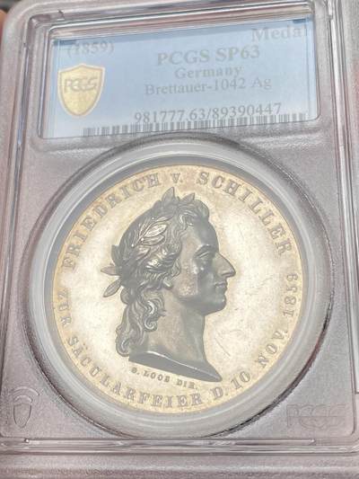 万国钱币拍卖第058期（万国新年大拍） PCGS MS63 1859年德国席勒诞辰百年纪念银章 PC唯一评级记录冠军分 稀见品种 43mm 28.8g 精制工艺强镜面，超高浮雕加厚盒。loos工坊大师炫技之作。雕刻细节极佳，人物栩栩如生。实物非常漂亮。正面:桂冠诗人席勒头像。背面:带翼缪斯女神手里拿着竖琴在天空飞行，13颗星星环绕。圣灵守护我们，灵魂也在其中徘徊。天使小翅膀灵动可爱又迷人。欧盟的盟歌欢乐颂为席勒于1785年创作的诗歌。