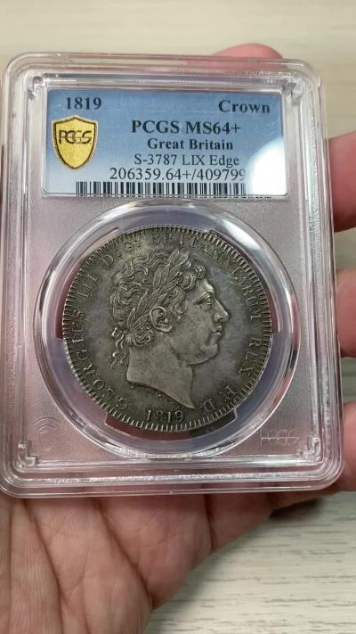 万国钱币拍卖第058期（万国新年大拍） PCGS MS64+ 1819年LIX英国乔治三世马剑克朗大银 英国马剑系列的开山之作 马剑图案由著名的意大利雕刻家Pistrucci设计 在钱币两面皆留下签名 这在当时是难以被接受的（通常只留首字母缩写） 此举也为后来首席雕刻师W.Wyon上位埋下伏笔 此枚无论底板，包浆，还是高点都堪称无可挑剔  一枚乔三马剑的标准器  高分价格越来越看不懂的存在 此次贴脸入手机会切勿错过
