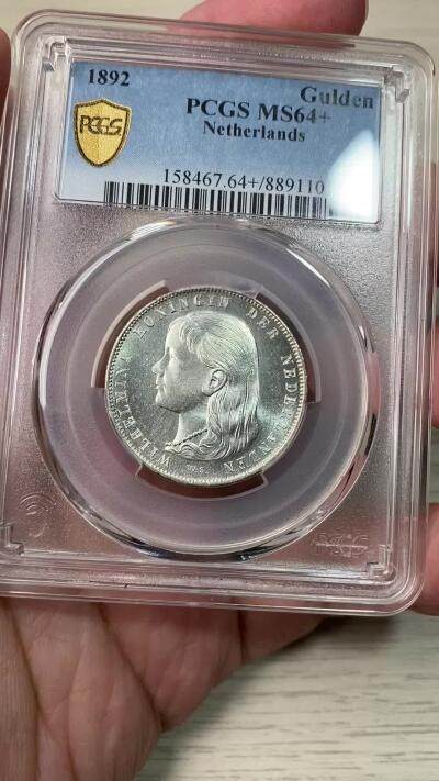 万国钱币拍卖第058期（万国新年大拍） PCGS MS64+ 1892年荷兰威廉明娜女王少女头像一盾银币 人见人爱的小萝莉。车轮霜光，打制极佳。底板类镜面质感，优异状态无愧一个加号，BU级别越来越难碰到了。瑞士拍卖NGSA刚拍的一枚66分到手约合RMB九万元。大热门品种，潜力十足，自藏级佳品。