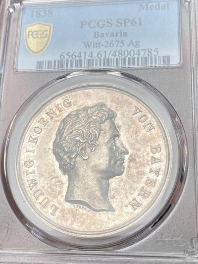 万国钱币拍卖第058期（万国新年大拍） PCGS SP61 1838年德国巴伐利亚路德维希一世奥格斯堡练兵营纪念景观大银章 罕见品种 超高浮雕 正面：拜仁国王路德维希头像 背面：奥格斯堡城市景观，城外原野景观。军营帐篷，各类武器，刀剑枪炮斧，盔甲大炮炮弹。 背面中央镶嵌了一块钴金属 仿佛天外来客 设计巧思 应该是唯一一个使用镶嵌工艺的老银章 亚军分自藏状态合格 高分难遇的品种 