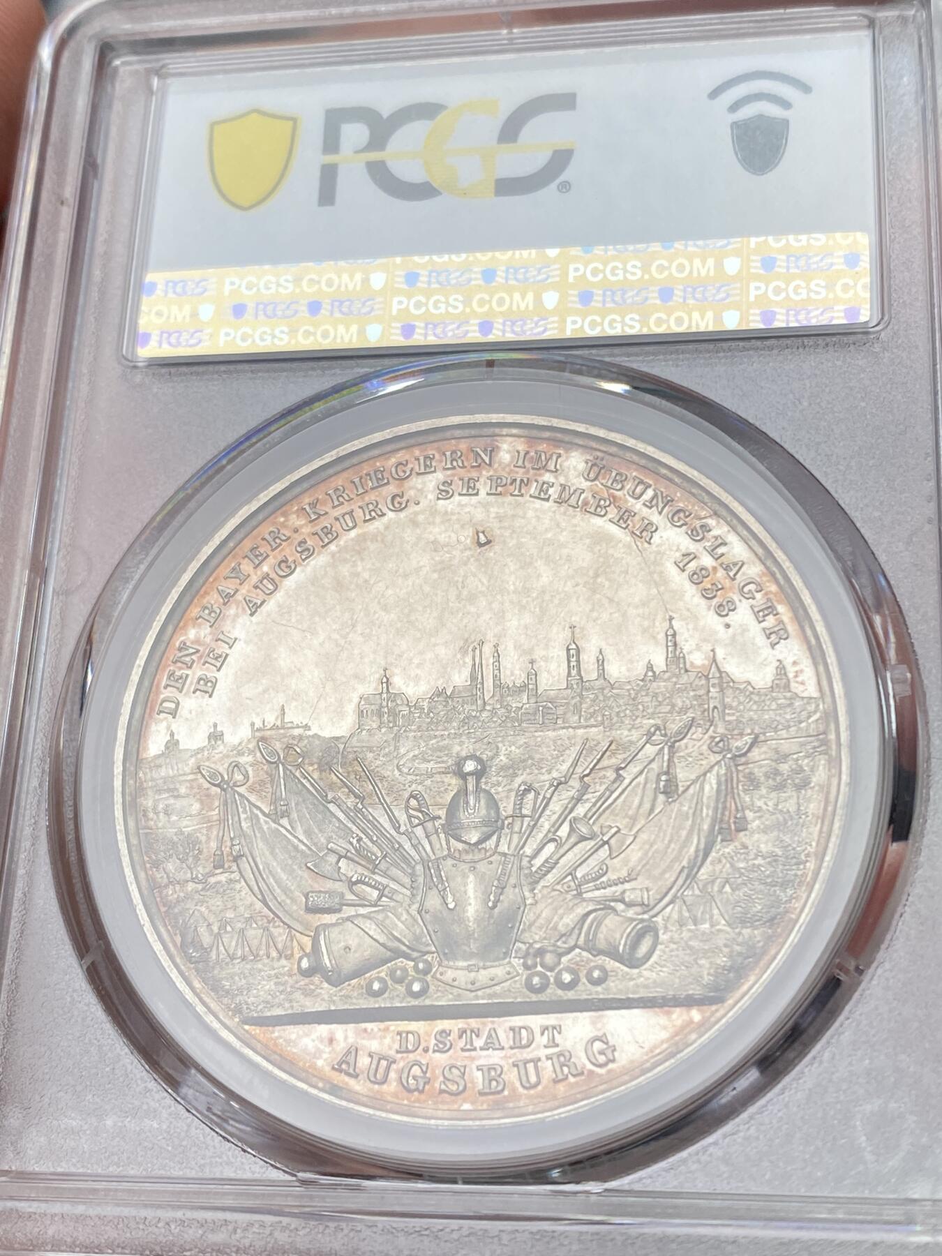万国钱币拍卖第058期（万国新年大拍） PCGS SP61 1838年德国巴伐利亚路德维希一世奥格斯堡练兵营纪念景观大银章 罕见品种 超高浮雕 正面：拜仁国王路德维希头像 背面：奥格斯堡城市景观，城外原野景观。军营帐篷，各类武器，刀剑枪炮斧，盔甲大炮炮弹。 背面中央镶嵌了一块钴金属 仿佛天外来客 设计巧思 应该是唯一一个使用镶嵌工艺的老银章 亚军分自藏状态合格 高分难遇的品种 