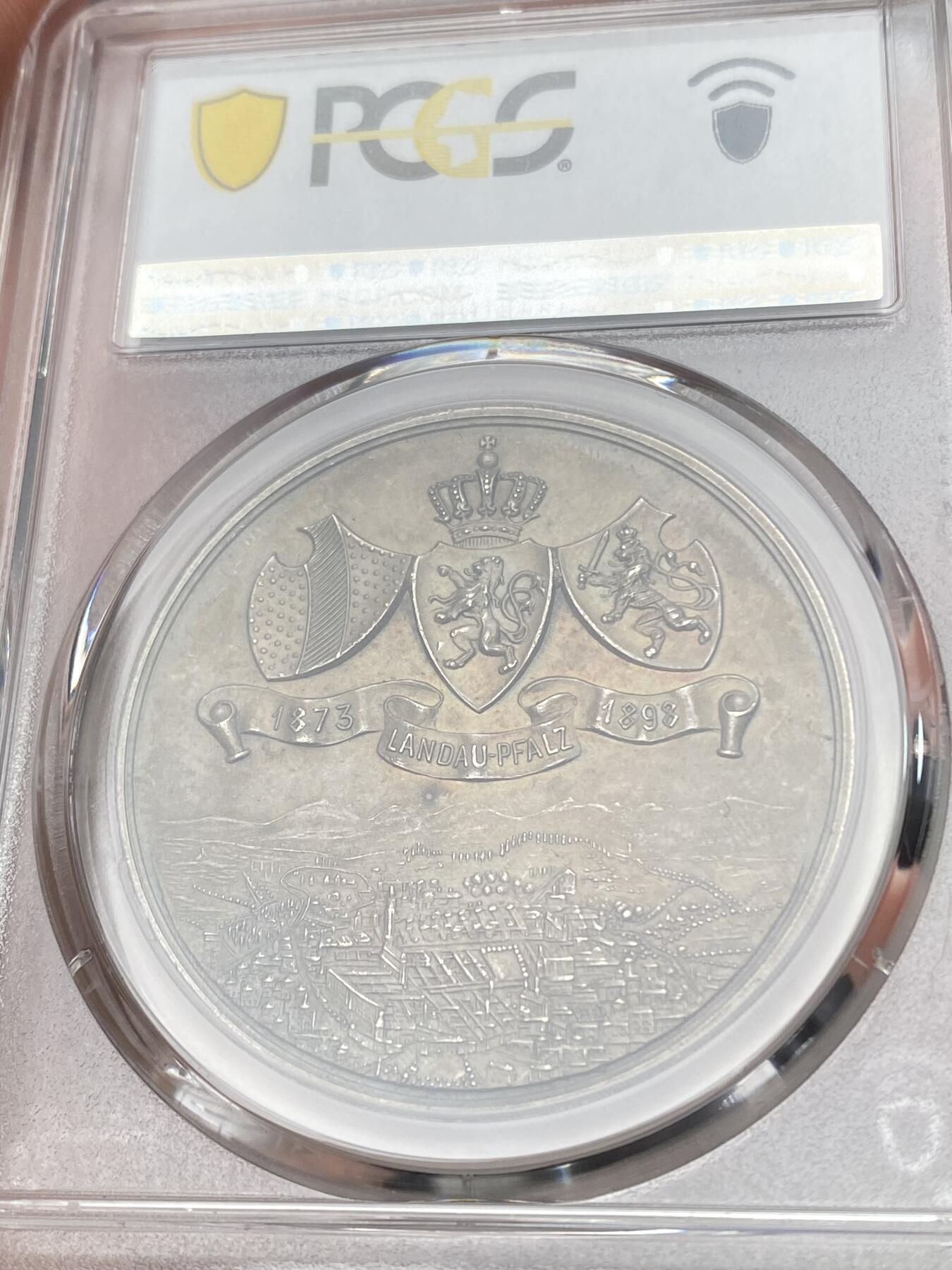 万国钱币拍卖第058期（万国新年大拍） PCGS MS63 1898年德国巴伐利亚兰道-普法尔茨第十六届射击节暨25周年纪念银章 冠军分罕见小邦射击节 正面:日耳曼妮娅女神右手举着胜利桂冠，左手持橡树枝，靠在兰道城市纹章盾徽上，巴伐利亚雄狮趴在她的脚边，底部是射击节标志。背面:王冠，巴伐利亚-兰道-普法尔茨的盾徽，底部是群山中的城市景观，朝阳升起。鸟瞰视角，广阔天地跃然章上。微缩雕刻，极其精细。高浮雕磨砂工艺，热门女神德射，自藏佳品。