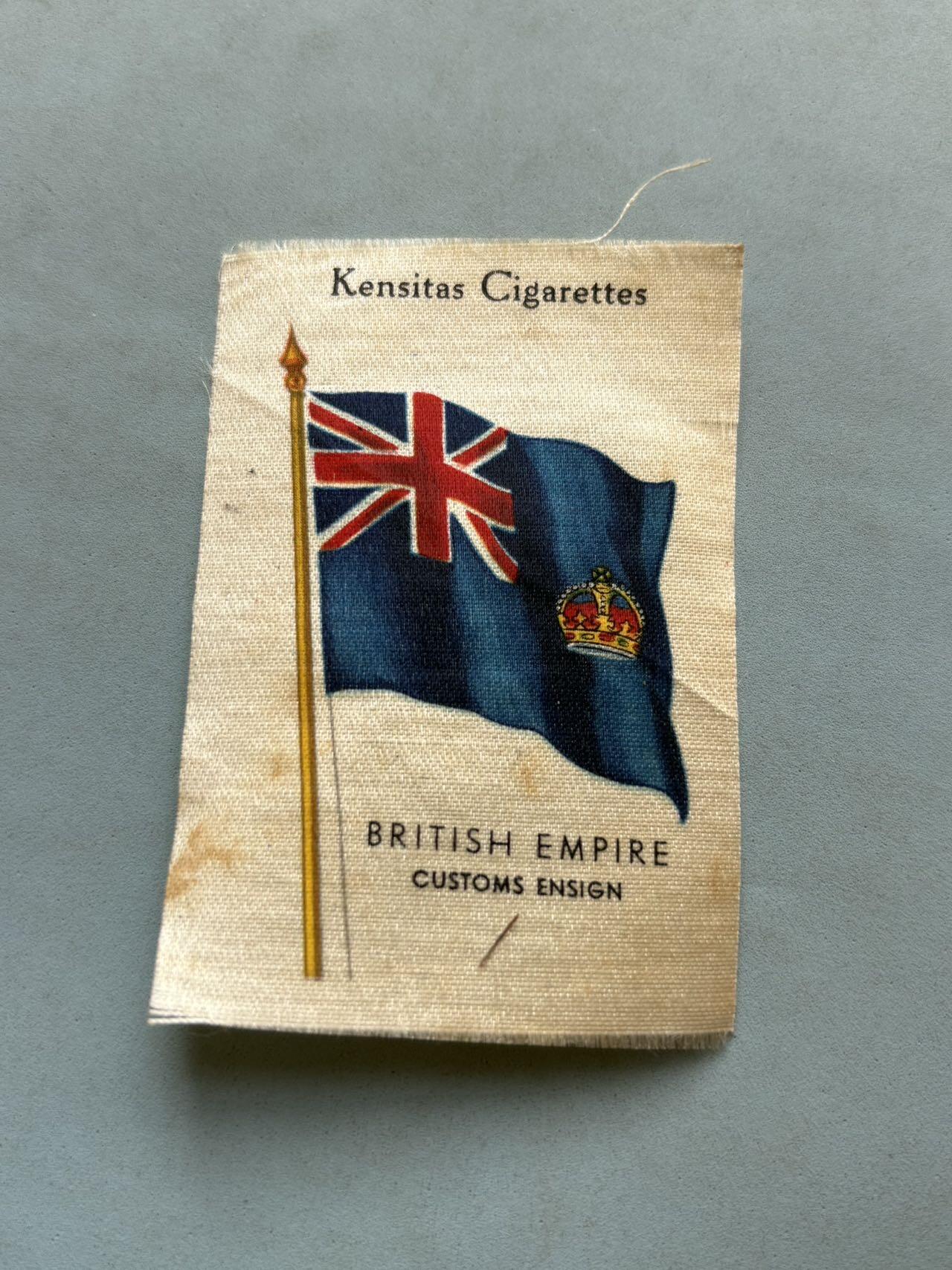 盛世勋华——号角文化勋章邮票专场拍卖第297期 1934年大英帝国海关旗主题丝绸收藏卡，尺寸约76mm×54mm， 以英国蓝船旗为基底，左上角是联合王国国旗（米字旗），右侧缀有皇家王冠纹章，是大英帝国时期海关船只的专用旗帜，体现了当时英国的殖民海事管理体系。