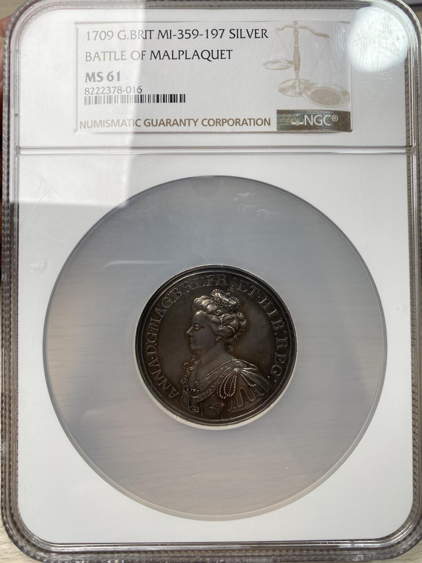 万国钱币拍卖第058期（万国新年大拍） NGC MS61 1709年英国安妮女王马尔普拉奎特战役纪念大银章 不列颠尼亚在天空中祝福军队 左边的发过军队在向进攻中的盟军开炮 宏大的英系早期战争场景刻画 细腻生动的细节刻画令人惊叹 原味黑彩收藏级品质（盒子背面有划痕）