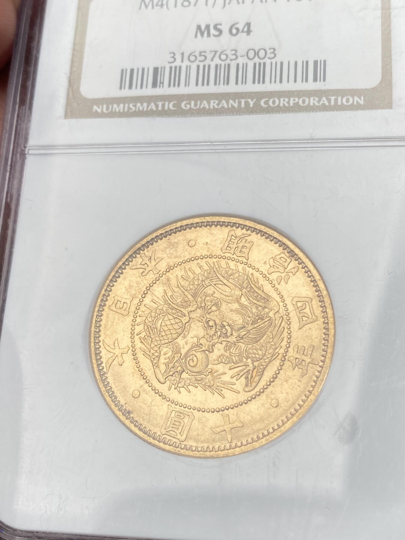 万国钱币拍卖第058期（万国新年大拍） NGC MS64 1871年日本明治四年双旗旧十円大金币 日系经典名誉品种 大阪造币厂铸 背面中央是日本传统神话中三神器之一的八尺镜 上方是象征日本皇室的十六瓣八重表菊纹 两边则是象征天照与月读大神的旗帜 也是明治四年发行货币中的最大面值 打制深峻丝绸金光轻微类镜面质感 NGC老白盒顶级收藏品质 16.66G 900金 