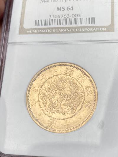 万国钱币拍卖第058期（万国新年大拍） NGC MS64 1871年日本明治四年双旗旧十円大金币 日系经典名誉品种 大阪造币厂铸 背面中央是日本传统神话中三神器之一的八尺镜 上方是象征日本皇室的十六瓣八重表菊纹 两边则是象征天照与月读大神的旗帜 也是明治四年发行货币中的最大面值 打制深峻丝绸金光轻微类镜面质感 NGC老白盒顶级收藏品质 16.66G 900金 