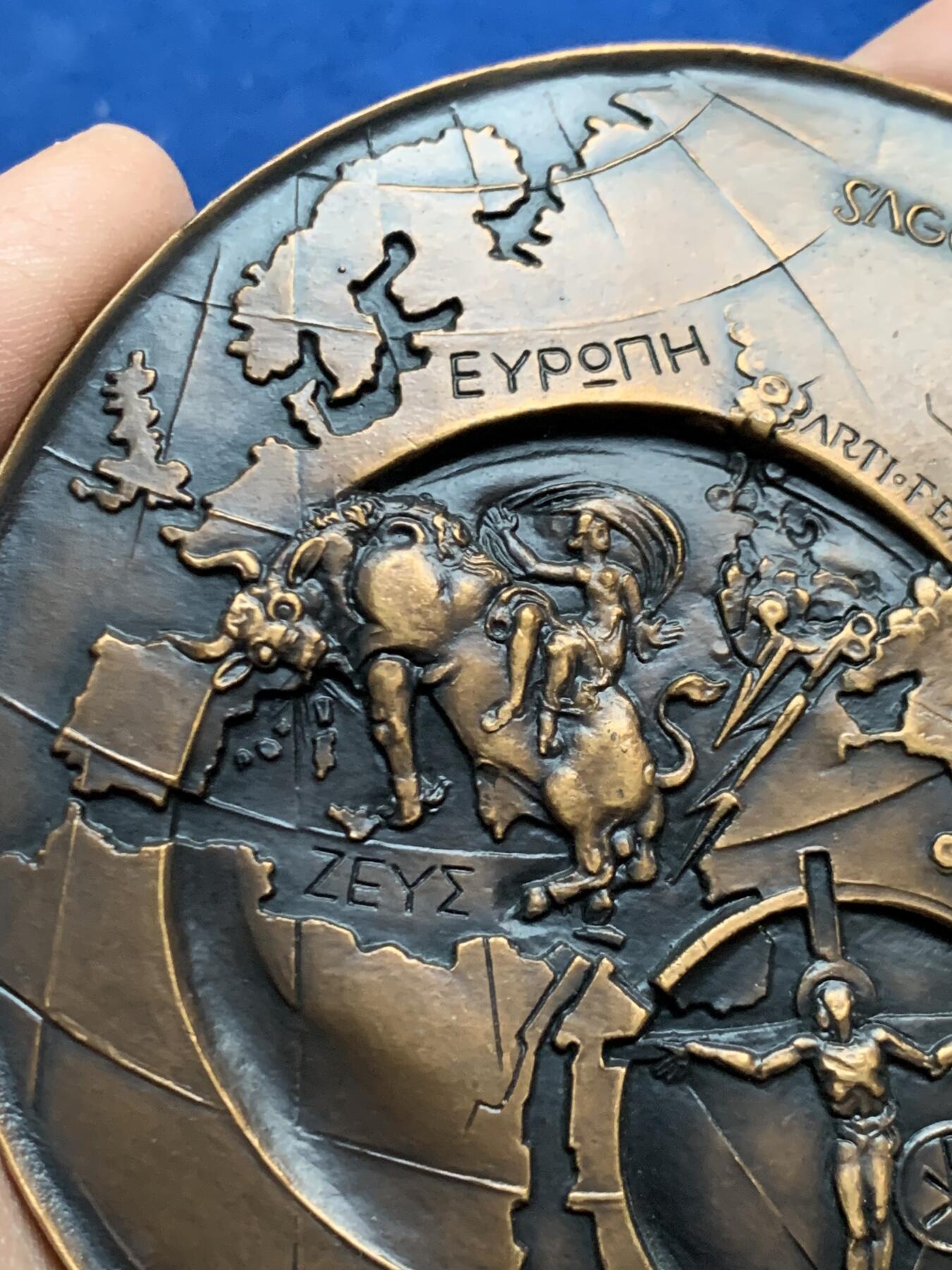 《竞宝斋》第452场 周日，周一 2场连拍 （全场包邮，欢迎送拍） 名家名作 德梅特尔·阿纳斯塔斯设计 迈向欧洲人文主义 超大号纪念铜章 506.5克，96.5mm，丰饶角铜标，此为原铸章， 市场出现大部分为边铭处带年份的后铸章  正面： 在地球仪上，描绘了宙斯化身为公牛掳走欧罗巴仙女的传说场景；下方圆形图案中为十字架上的基督及其花押字   背面：在欧洲地图上，三位分别代表地下、陆地与太空领域的主宰者。圆形图案中，两人在象征欧洲的树下握手，下方是希望之舟。