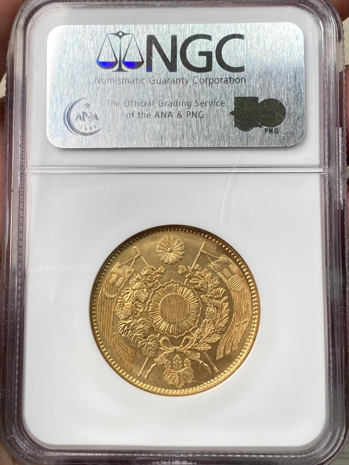 万国钱币拍卖第058期（万国新年大拍） NGC MS64 1871年日本明治四年双旗旧十円大金币 日系经典名誉品种 大阪造币厂铸 背面中央是日本传统神话中三神器之一的八尺镜 上方是象征日本皇室的十六瓣八重表菊纹 两边则是象征天照与月读大神的旗帜 也是明治四年发行货币中的最大面值 打制深峻丝绸金光轻微类镜面质感 NGC老白盒顶级收藏品质 16.66G 900金 