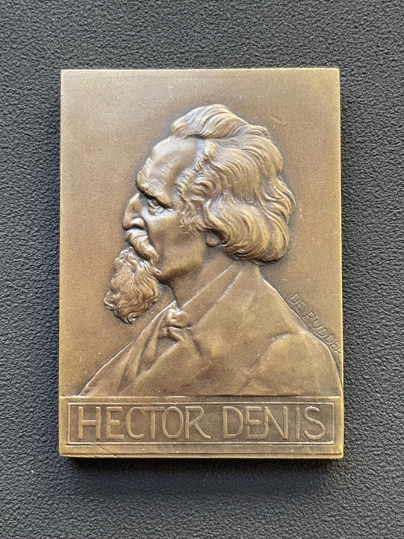 「木头集藏」章牌专场-第65场 比利时布鲁塞尔自由大学教授赫克托·丹尼斯纪念章， 尺寸：59×42mm，81.5g。 赫克托·丹尼斯教授于1878年至1912年间，在自由大学担任教职34年。这枚长方形铜章就是为纪念他的卓越奉献而定制的。 正面是教授的左侧胸像，下方铭文是他的姓名。背面为知识女神点向象征光明的太阳图案，上方三行铭文意为“自由大学”“教授”“1878年至1912年”。