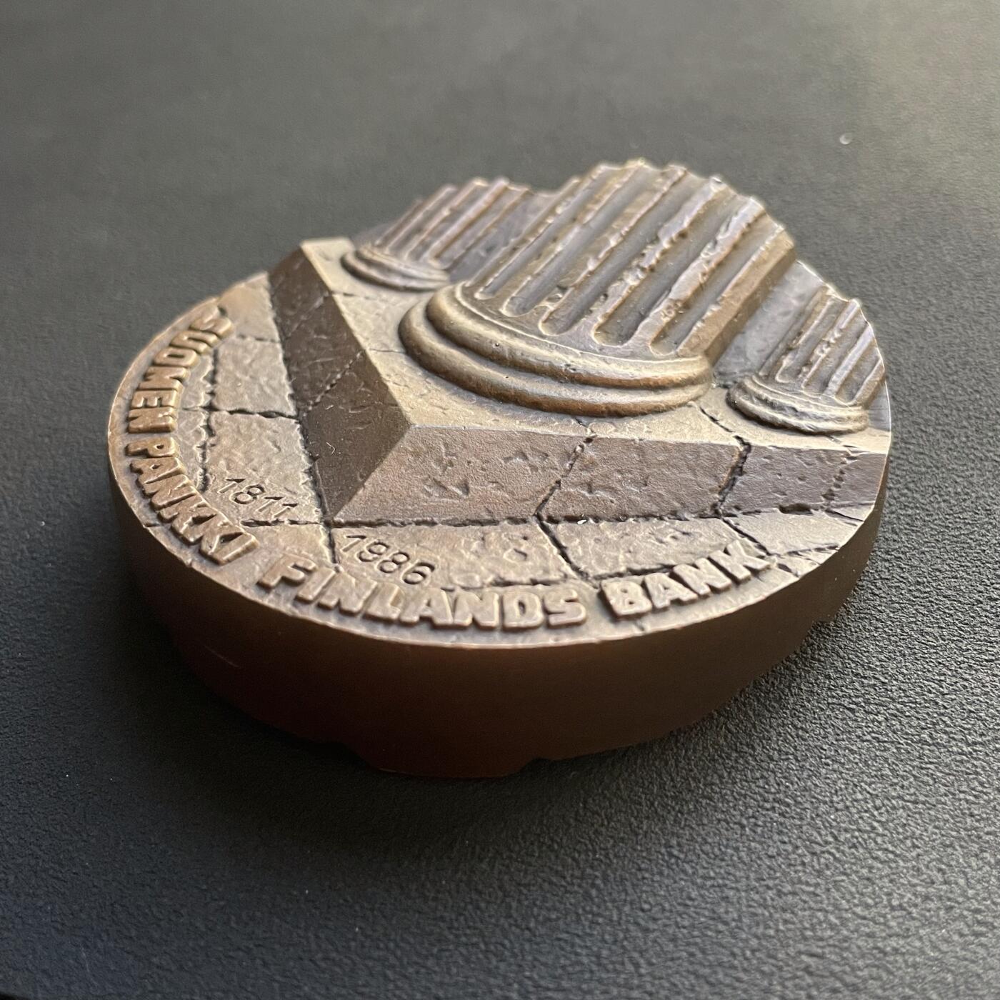 「木头集藏」章牌专场-第65场 芬兰银行（芬兰中央银行）175周年纪念加厚纪念大铜章，直径：70 mm，403g，特别加厚，超高浮雕，厚重压手。正面图案为高浮雕罗马柱基座，象征央行是芬兰国家的重要支柱基础。背面是抽象的芬兰地图高浮雕造型。 芬兰银行是芬兰共和国的中央银行，也是欧洲中央银行系统的成员。
